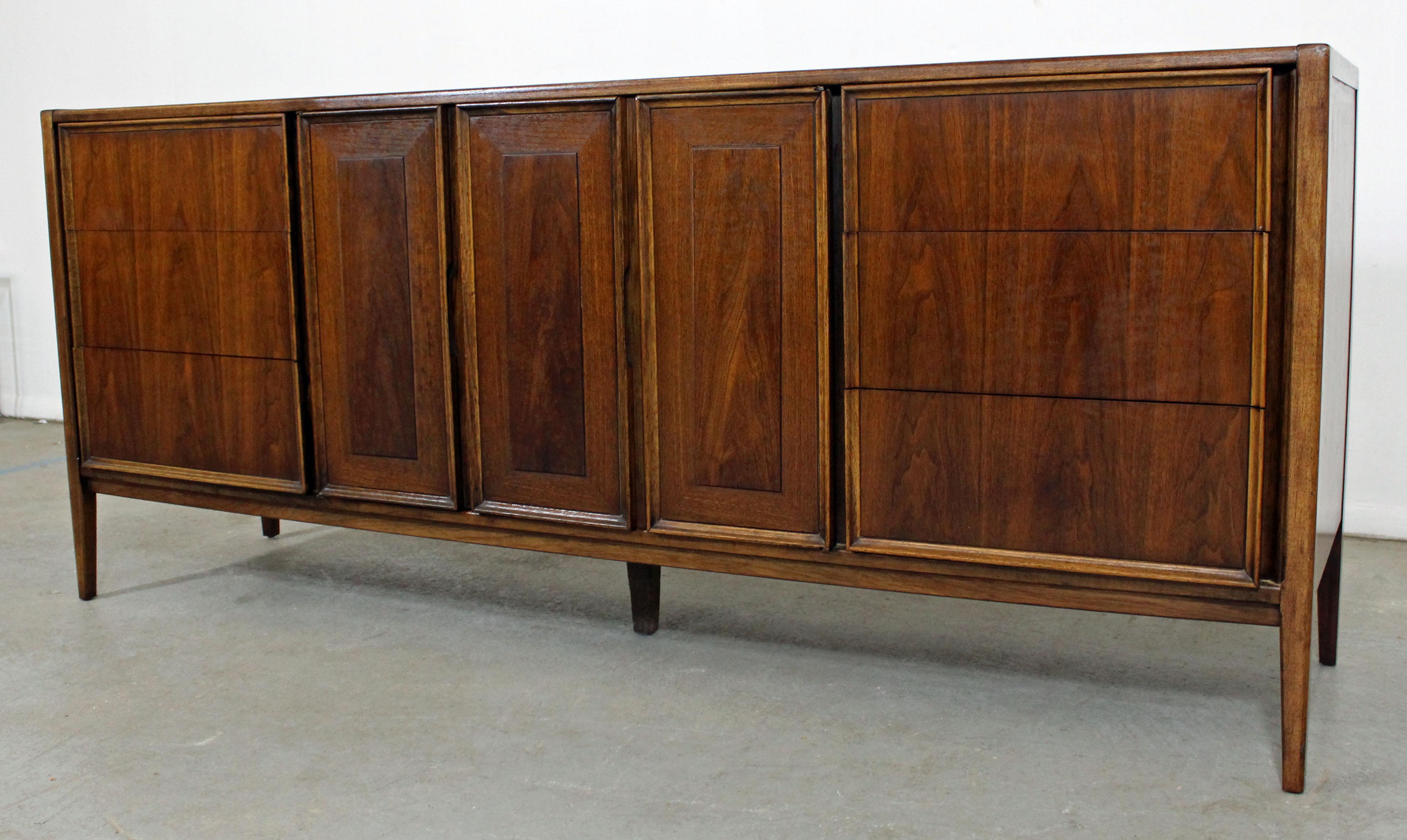 Offered is a Mid-Century Modern walnut credenza or dresser. Includes three drawers on each side and three center drawers behind three doors (2 bi-folding). Top drawer has a divider. It is in excellent condition for its age, has been refinished. It