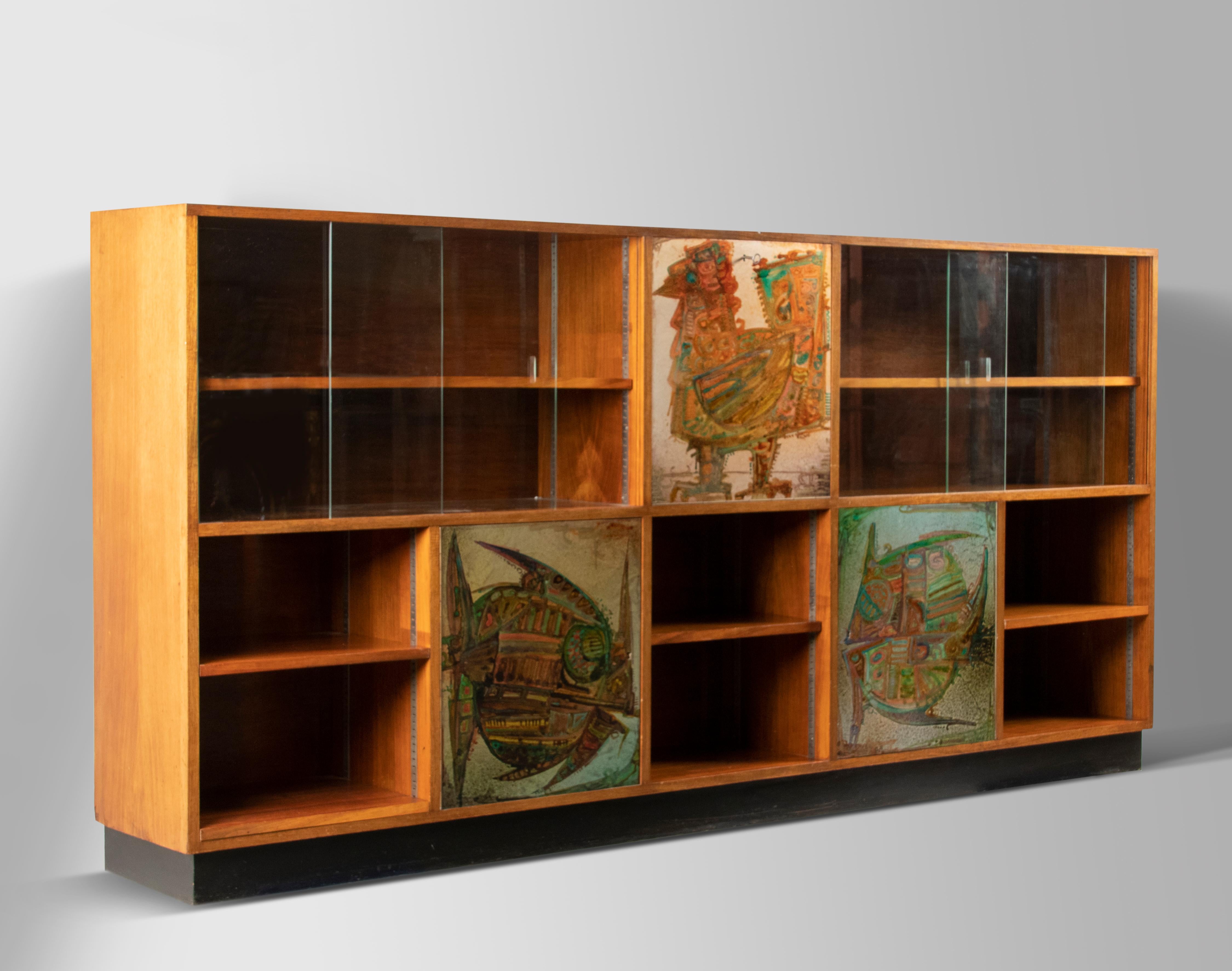 A long mid century bookcase made of walnut veneer. The cabinet has three aluminum painted panels with fishes. Created and signed and dated (1966) by Hubert Minnebo (Belgium, 1940). The cabinet has 3 doors. Left and right are glass sliding doors. The