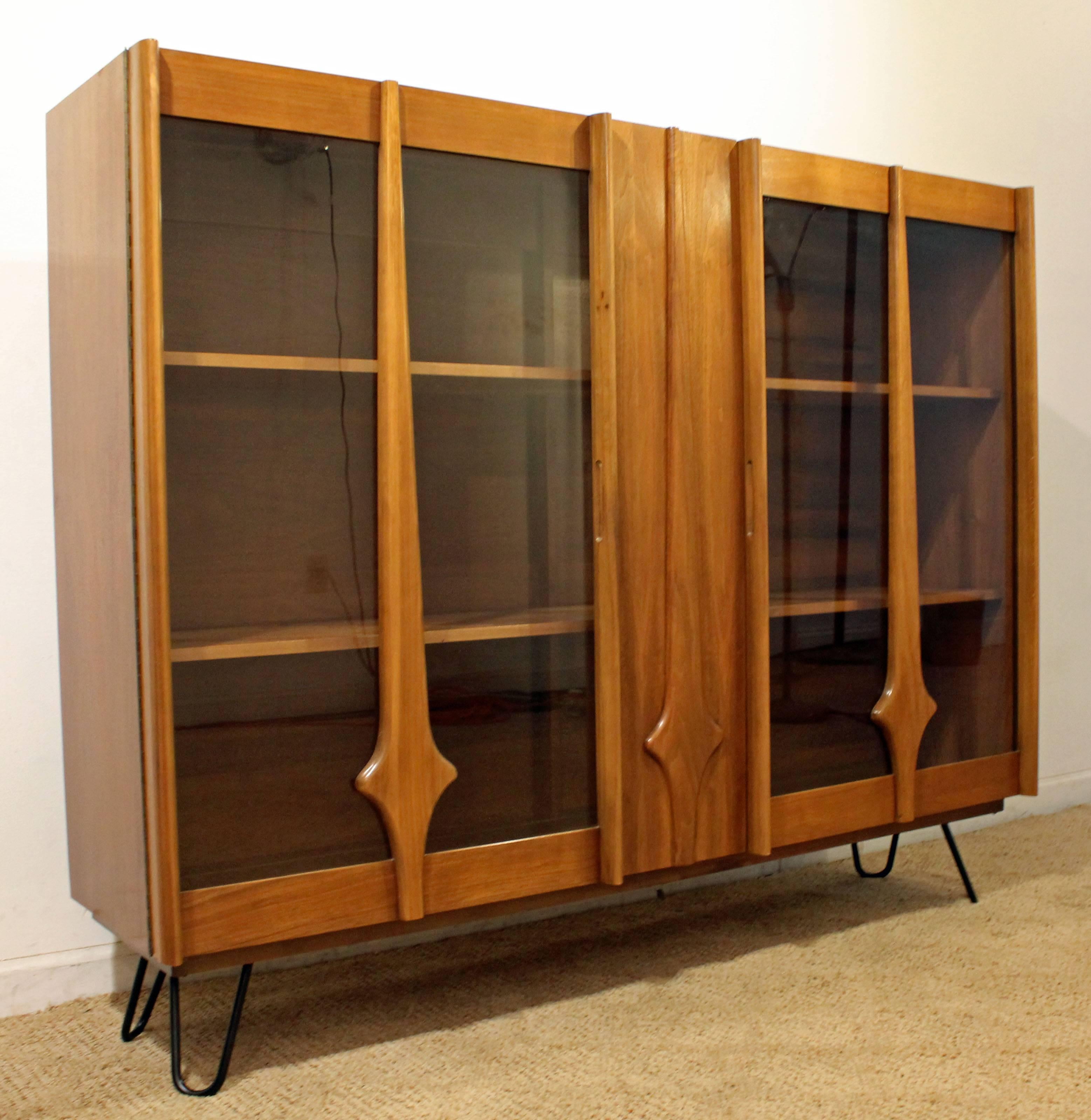 The piece is made of walnut, featuring two glass doors with shelving. This was a hutch top that has been attached to metal hairpin legs.

Dimensions:
60