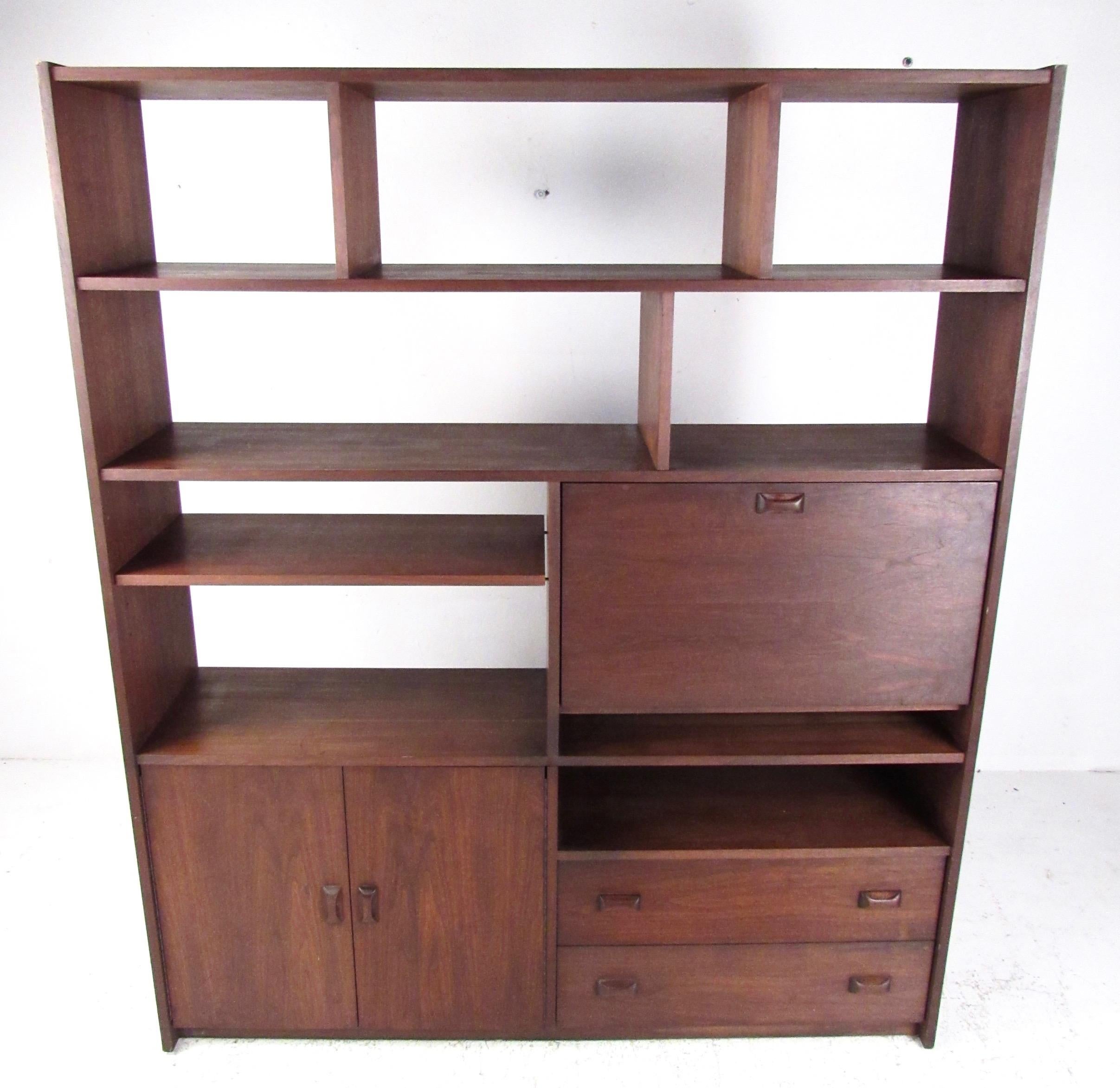 This impressive large scale bookshelf offers spacious storage options ranging from open shelves to cabinet storage and including a drop front workspace/bar cabinet. Carved wood pulls add even more mid-century modern appeal to the cabinets, doors,