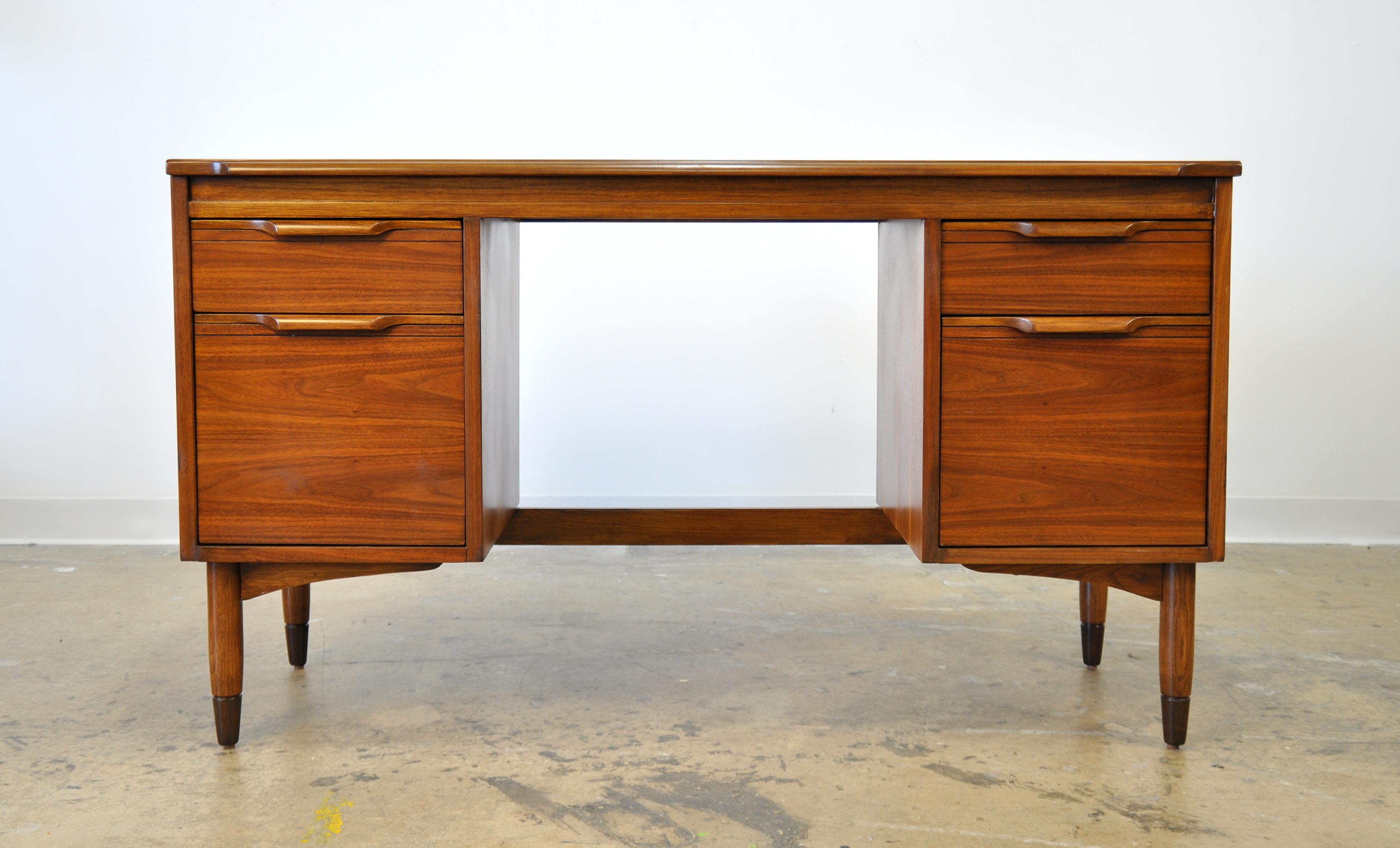 A vintage midcentury walnut desk or vanity table dating from the 1950s. Features a boat shaped or boomerang top with overhang. The shaped front sits over two drawers and two deep drawers. The drawer fronts have sculpted handles. The back side of the