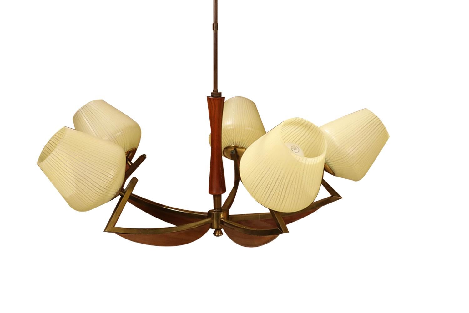 Impressive Mid-Century Modern five-arm chandelier. Features five frosted, ribbed style glass, conical taper shades, supported by curved brass arms, accented with crescent form walnut wood, extend under each arm, attached to a central brass final,