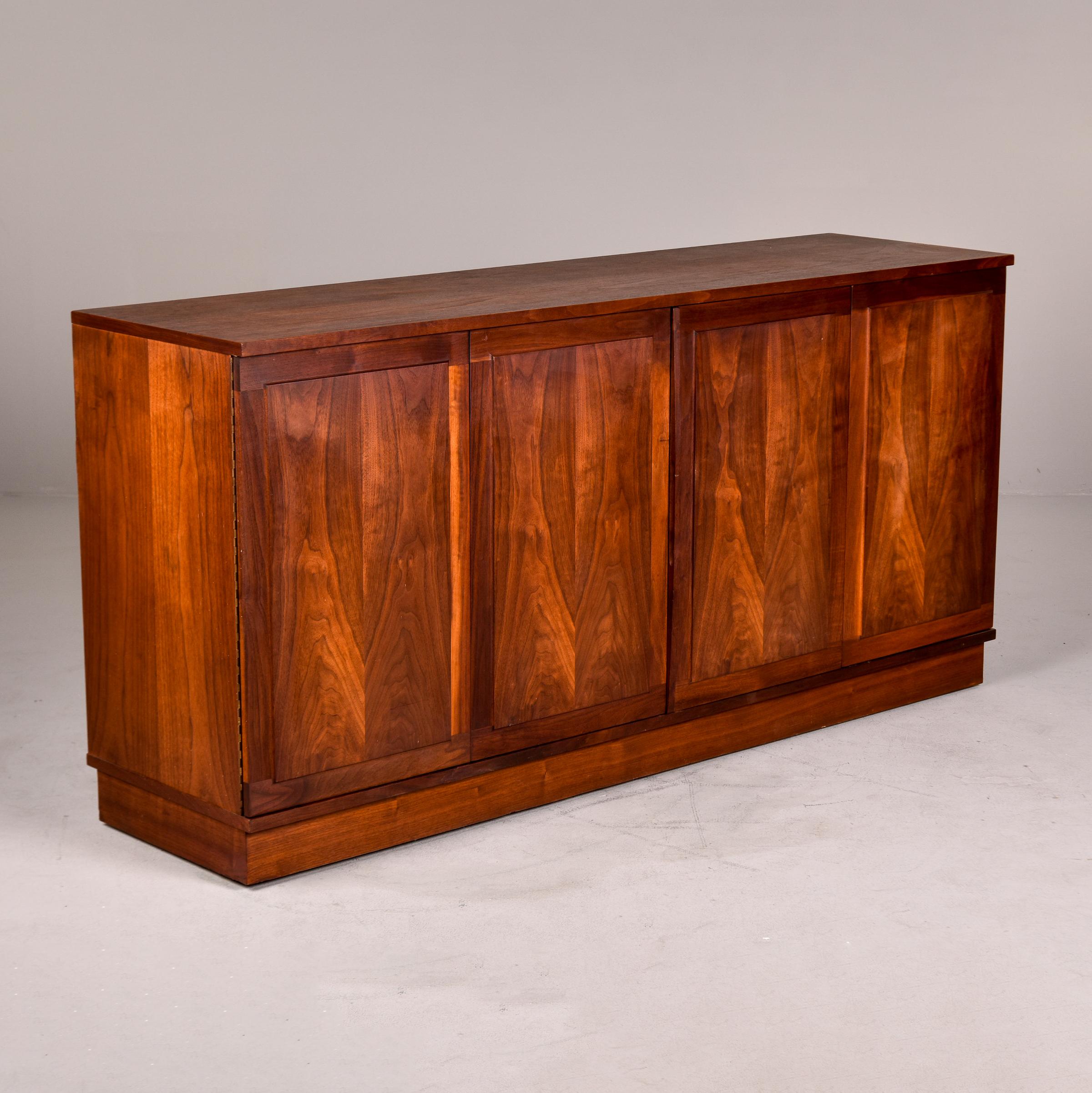 Found in the USA, this mid century walnut buffet dates from the 1960s. Four door panels are beautifully figured. Two doors of two panels each open to a lot of internal storage. Middle section has two wide, slender drawers with a single adjustable