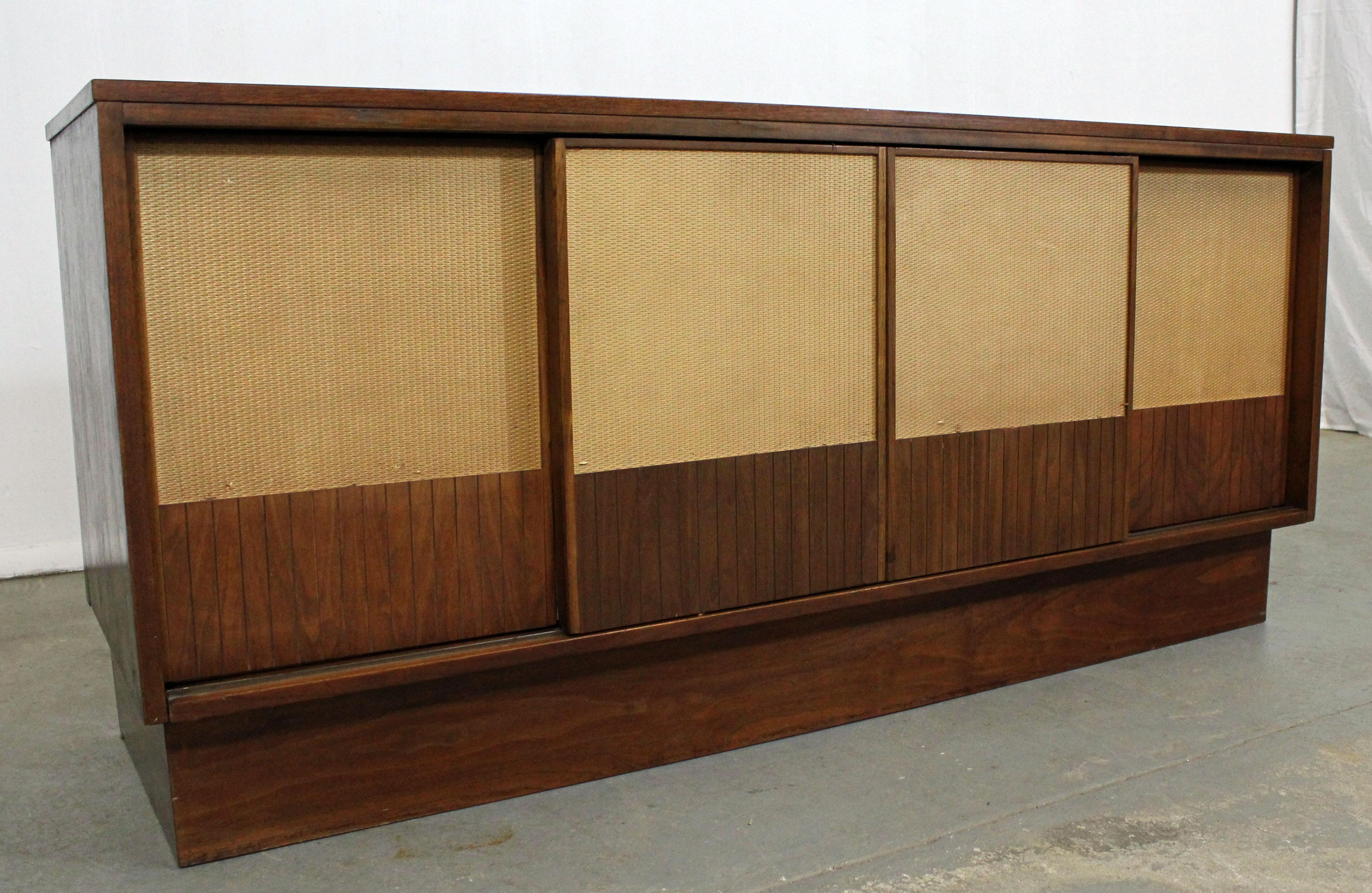Offered is a Mid-Century Modern customized walnut credenza, featuring four caned sliding doors with inside storage. This piece has been converted into a media console/record player stand by the previous owner. Inside has various shelving and a pull