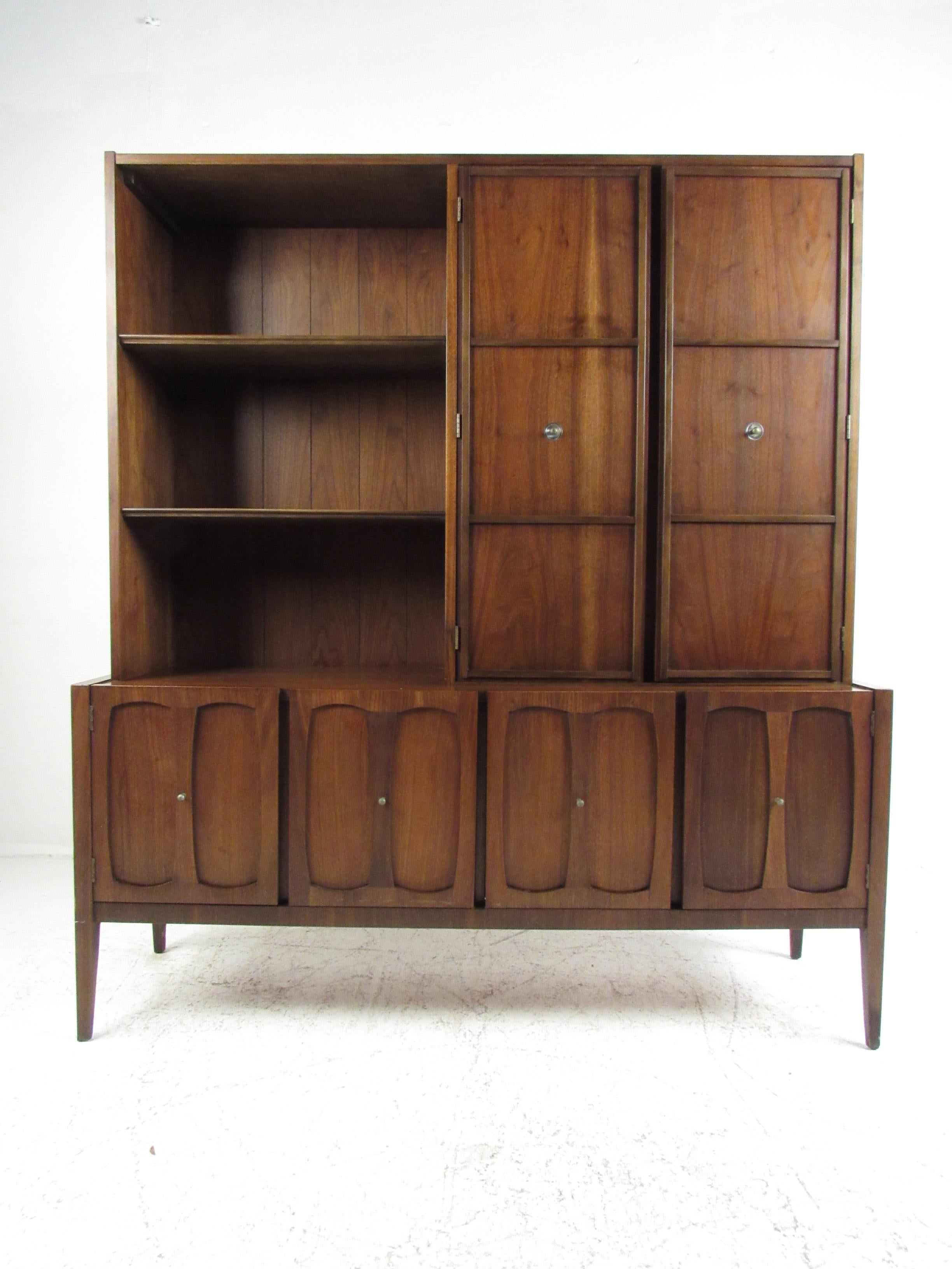 This stunning vintage modern china cabinet features unique carved designs on cabinet door fronts and sculpted pulls. A well-made case piece that functions as a buffet, bookcase, or display case. Sleek design with tapered legs, an elegant walnut