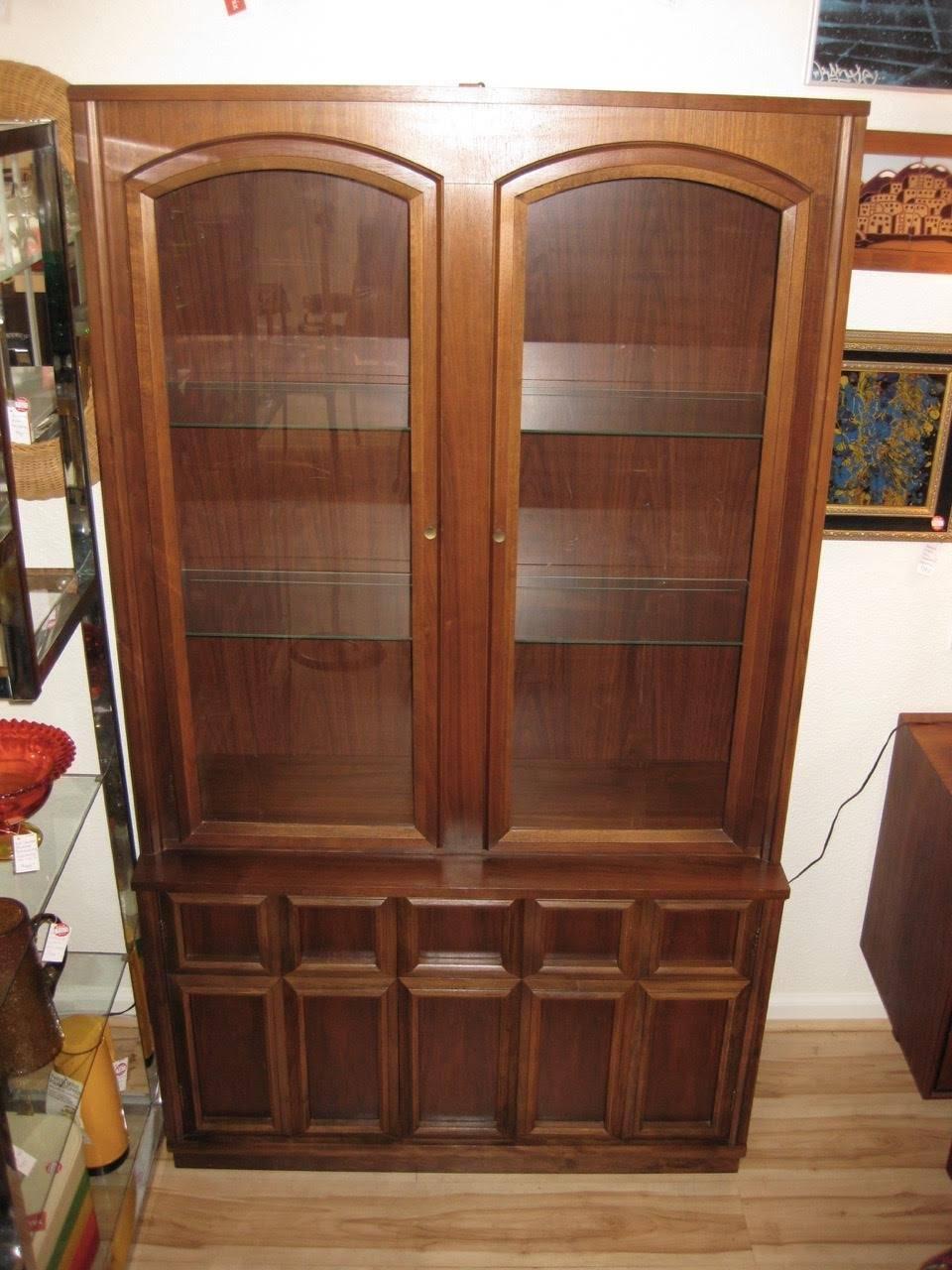 Mid-Century Modern walnut china hutch or cabinet. Cabinet has two glass doors on upper cabinet with two glass shelves with grooved tracks for plate display and light. Panelled base has two doors with a shelf on one side and drawer on other
