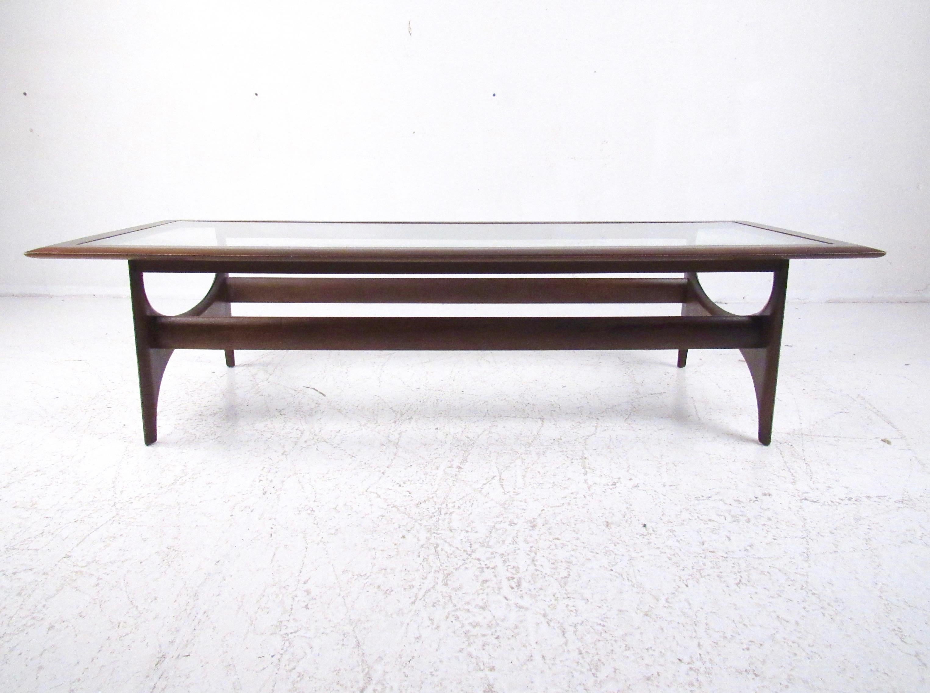 This striking walnut finish coffee table features a glass top and stylish Mid-Century Modern design. Simple yet unique design by Lane Furniture makes an impressive centre table for home or business seating arrangement. Please confirm item location