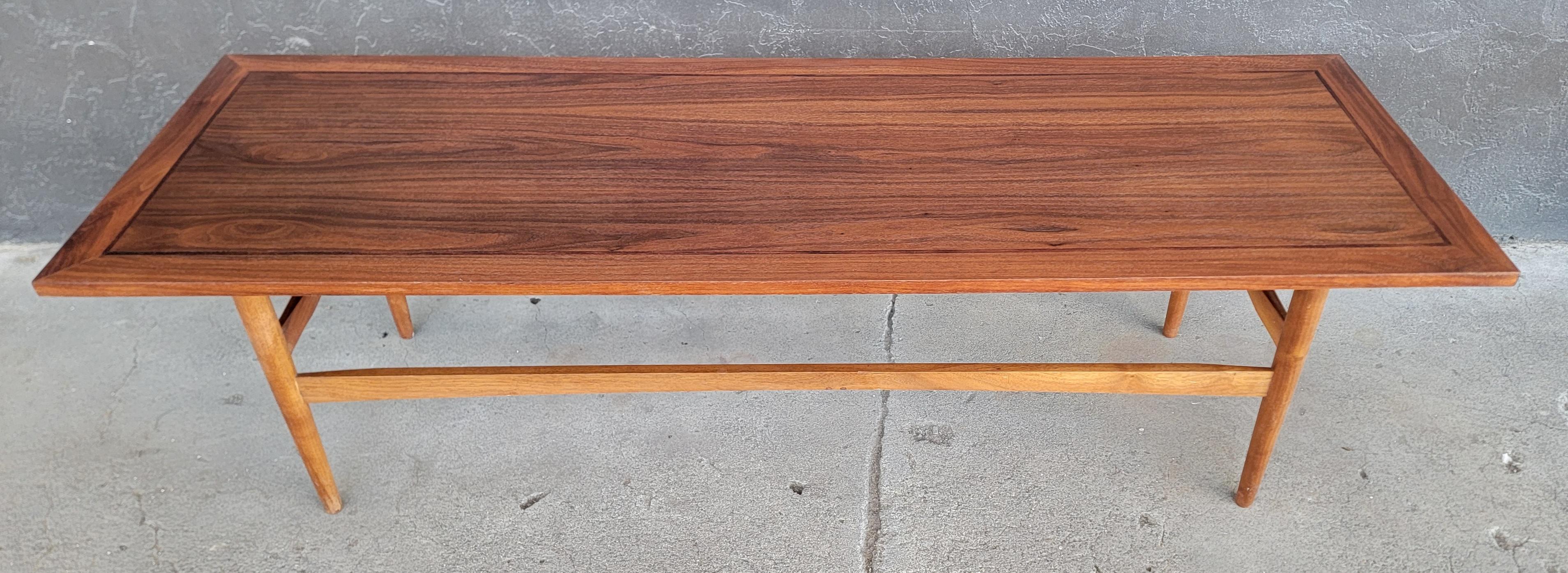 A classic, good ole fashion mid-century modern rectangular coffee table. Nice walnut wood grain with a an unusual rosewood inlay band. Peg legs.  Refinished. 

59.5 inches wide.
19.75 inches deep.
17.25 inched high.