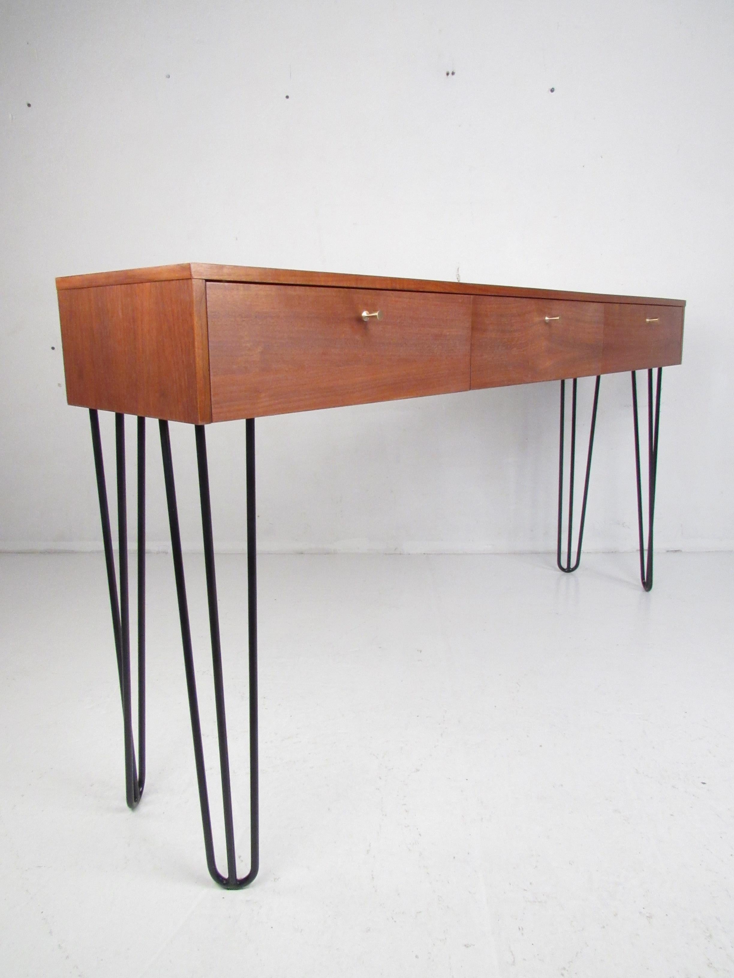 This versatile midcentury vanity features three drop front storage compartments and large metal hairpin legs. A stylish piece that functions as a small desk, vanity, or a hall table. This lovely vintage modern table looks great in any bedroom,