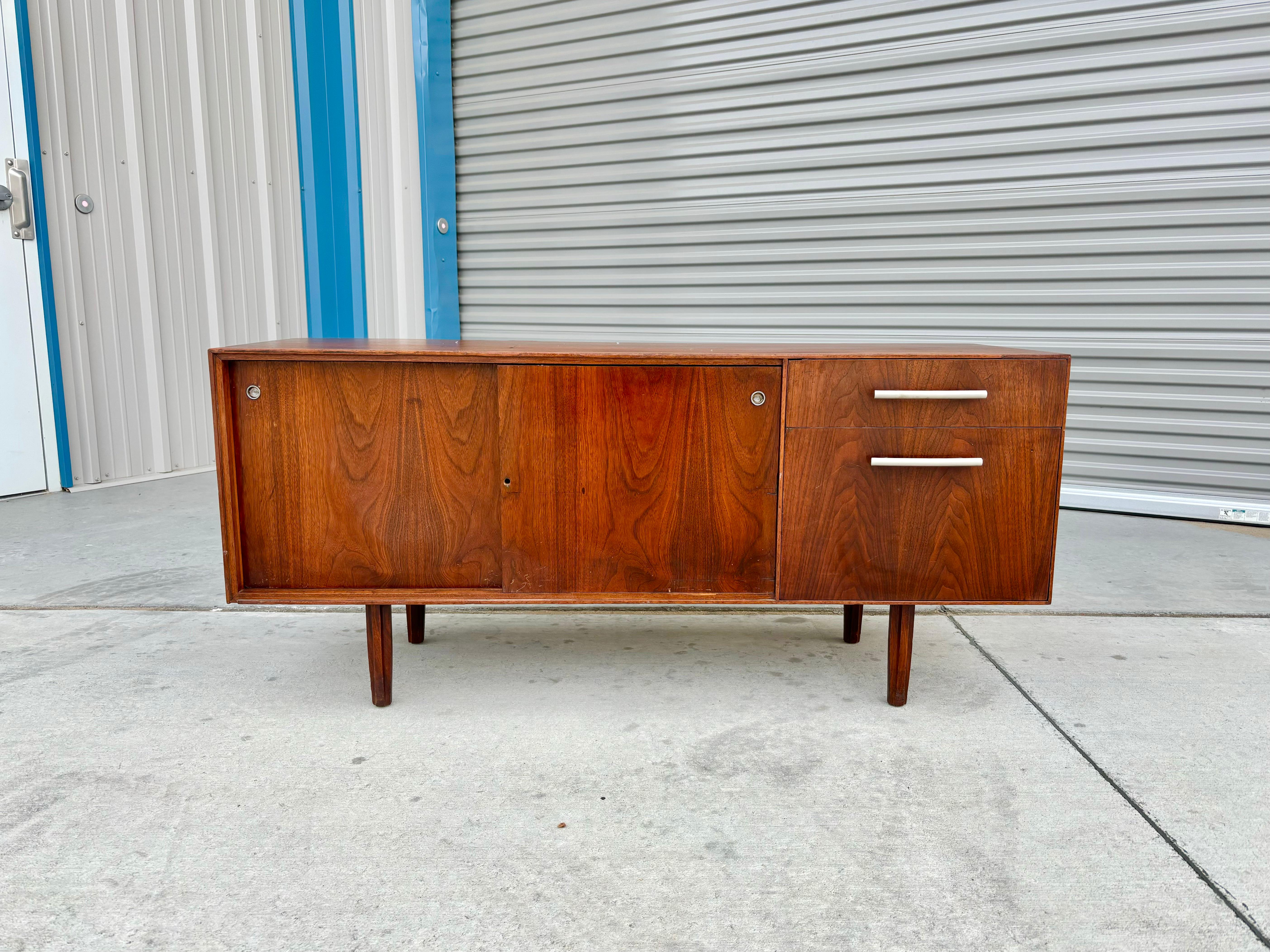 Mid-century walnut credenza designed and manufactured in the United States in the 1960s. This exquisite piece boasts a gorgeous walnut frame that is both durable and stylish. On the right side, you'll find two convenient pull-out drawers that glide