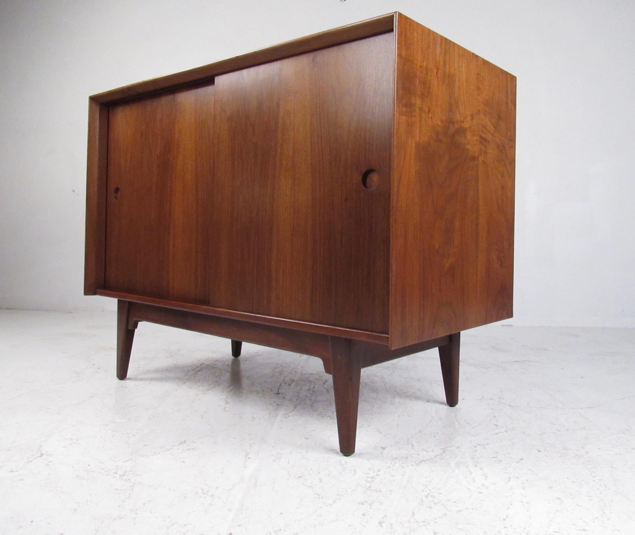 This petite Mid-Century Modern credenza features rich walnut finish and sturdy construction. Spacious interior cabinet features adjustable shelves offering versatile storage space in a stylish vintage credenza. Ideal piece for office storage or use