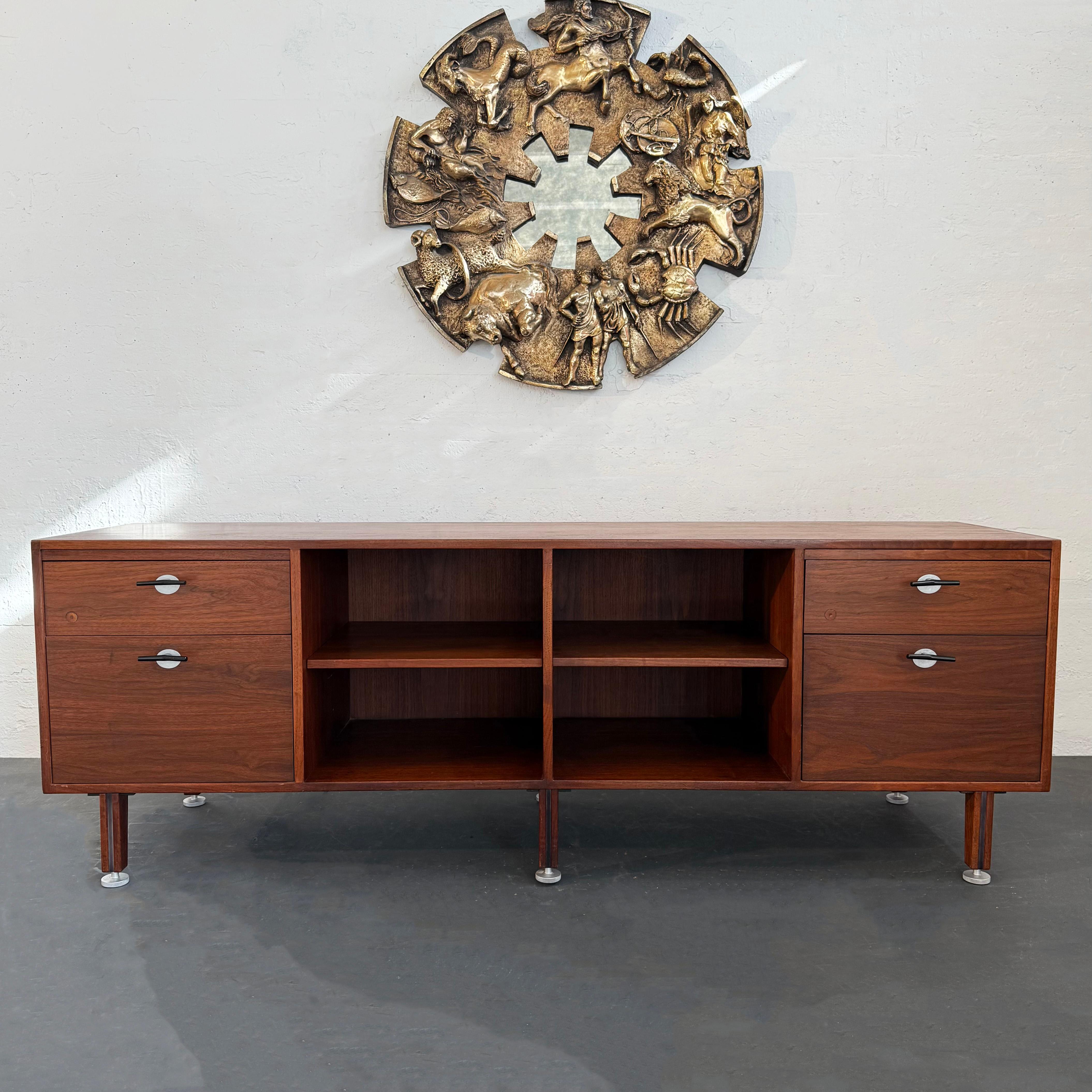 This walnut credenza bookcase is designed by Danish American designer Jens Risom for Jens Risom Designs. It features drawers with his signature steel Y shaped pulls and open shelves in the center for books or display. The 7.5 inch height legs have a
