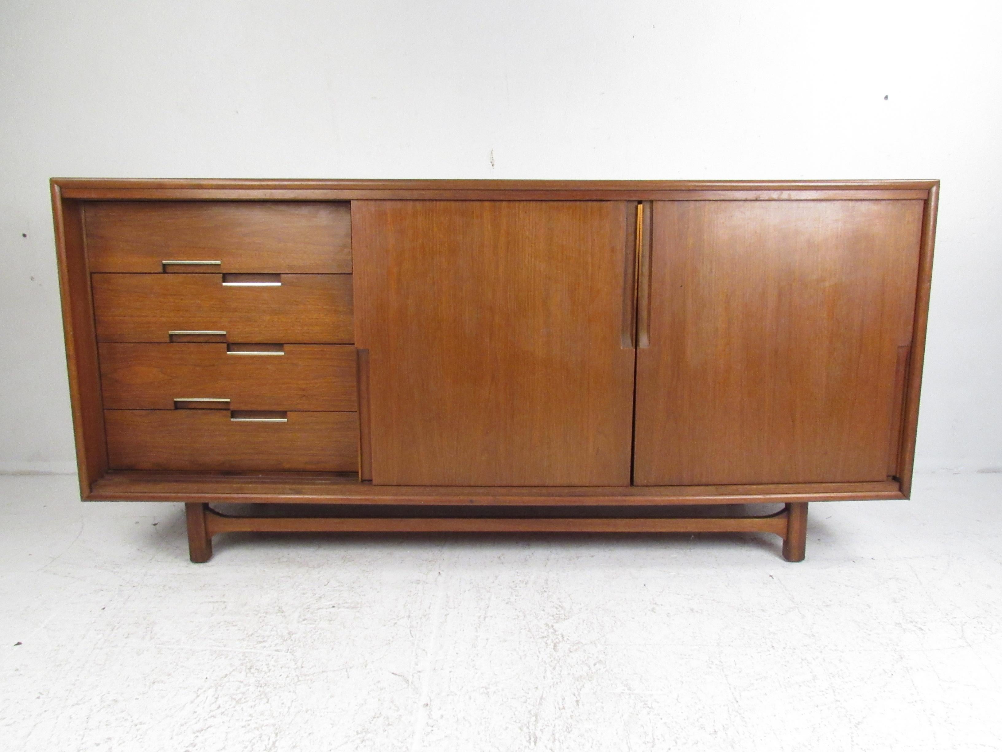 This attractive vintage modern walnut credenza features nine hefty drawers hidden by unique sliding doors. Sleek design with recessed drawer pulls, dovetail joints, and a sculpted stretcher along the base. Quality construction on display that offers