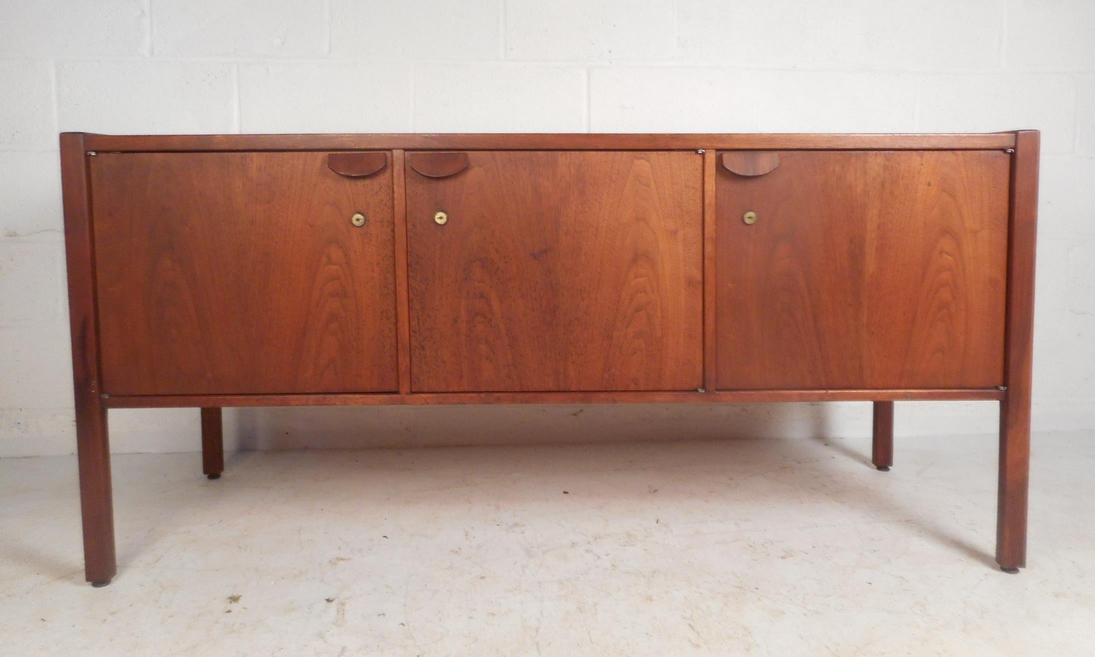 A beautiful vintage modern dark walnut buffet with three cabinet doors hiding an abundance of storage space. A sleek design by Jens Risom with straight lines, sculpted pulls, and elegant walnut wood grain throughout. A handsome midcentury case piece