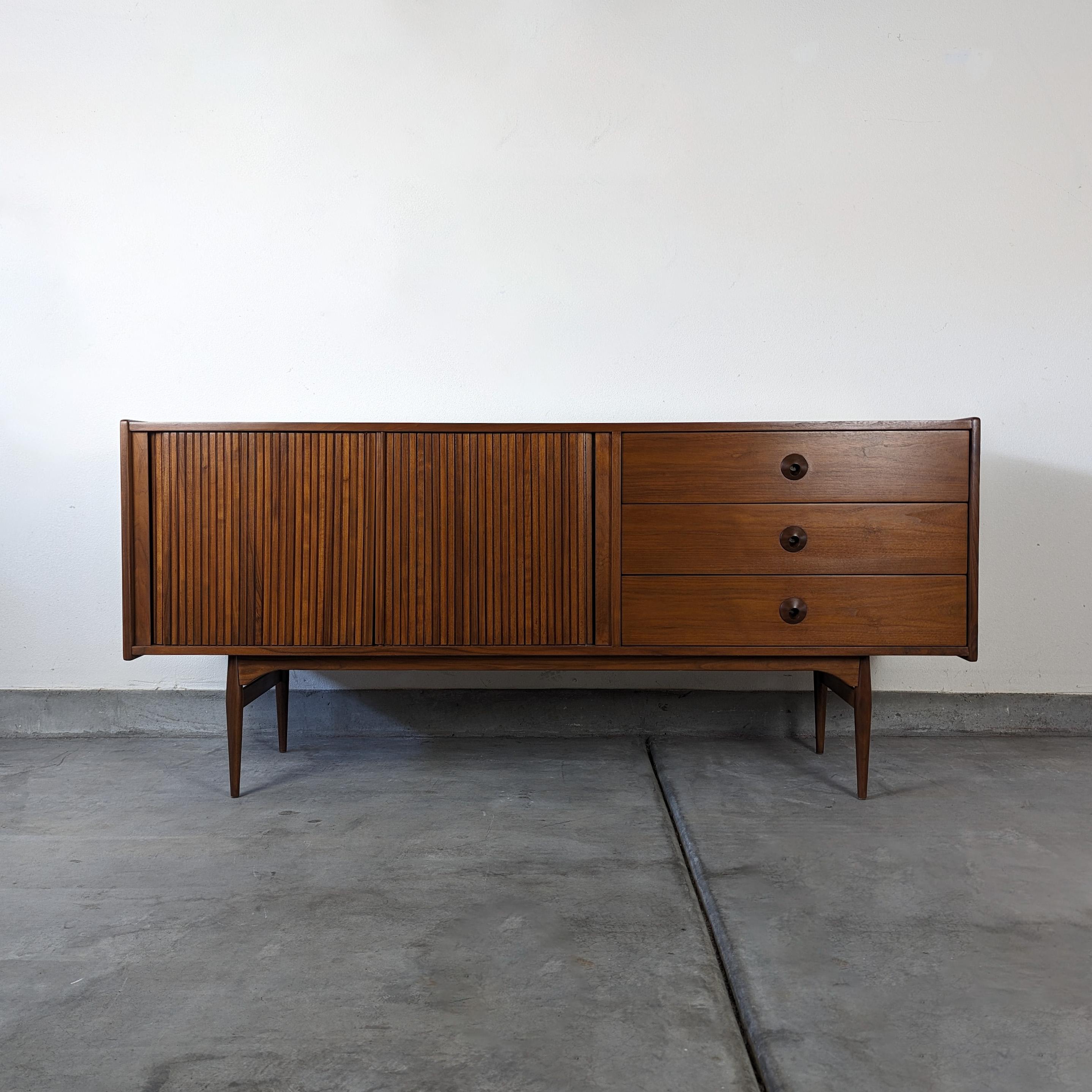 Introducing the epitome of mid-century modern elegance! This exquisite tambour door credenza, designed by John Keal & expertly manufactured by the renowned furniture brand Brown Saltman, is a true testament to timeless design and impeccable