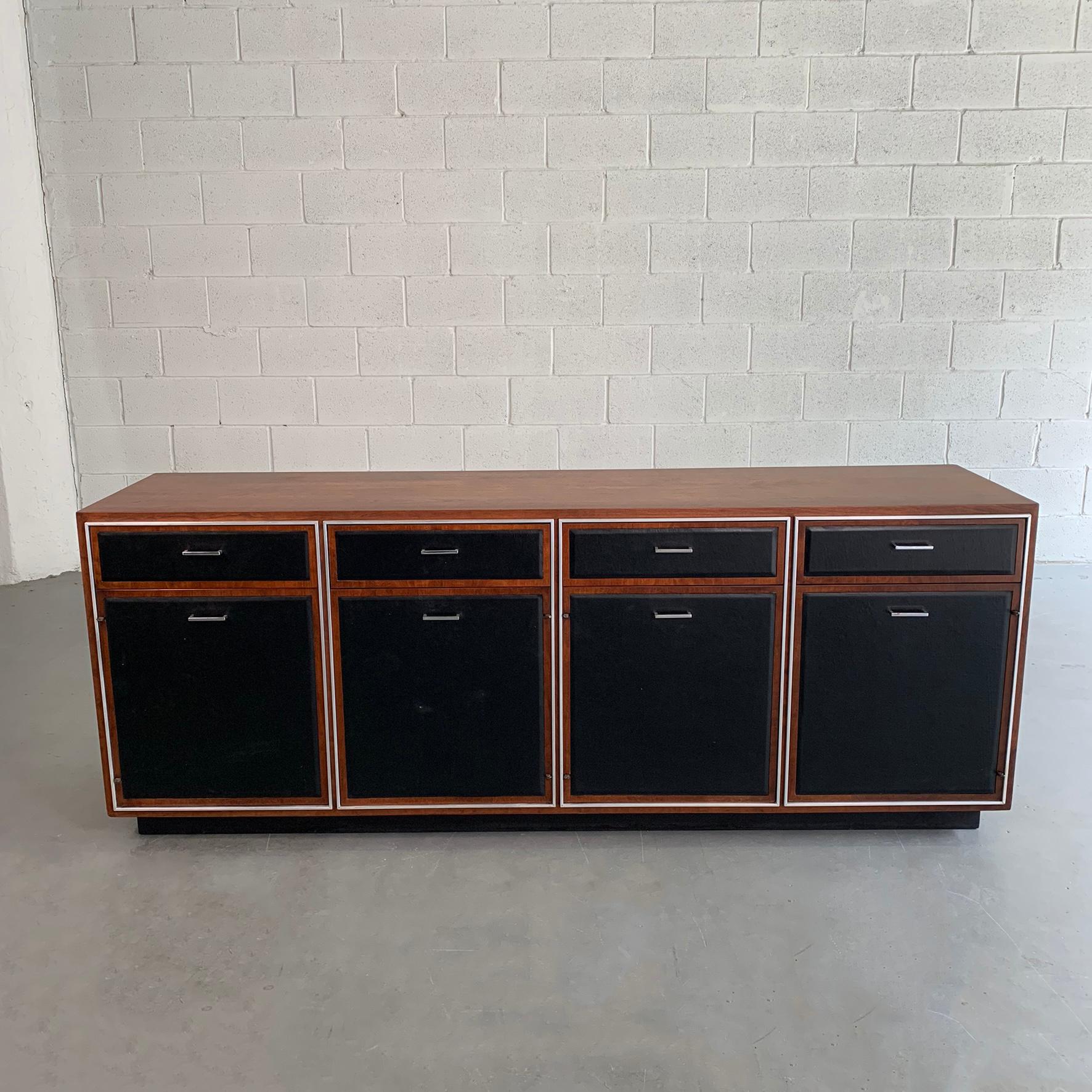 Mid-Century Modern credenza by John Stuart features a crotch walnut surround and vinyl covered drawer and door fronts with aluminum trim and handles. The bottom cabinets are 18 W x 18 D x 19 H.