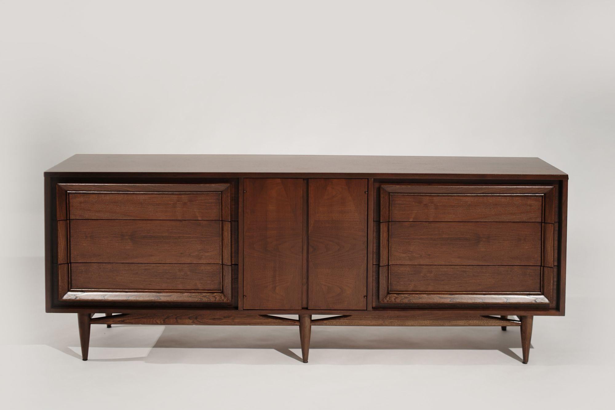 A Mid-Century Modern walnut dresser expertly restored by Stamford Modern. Features six large drawers and bookmatched center doors that open to reveal three smaller drawers. Its sleek design and rich walnut grain make it a timeless addition to any
