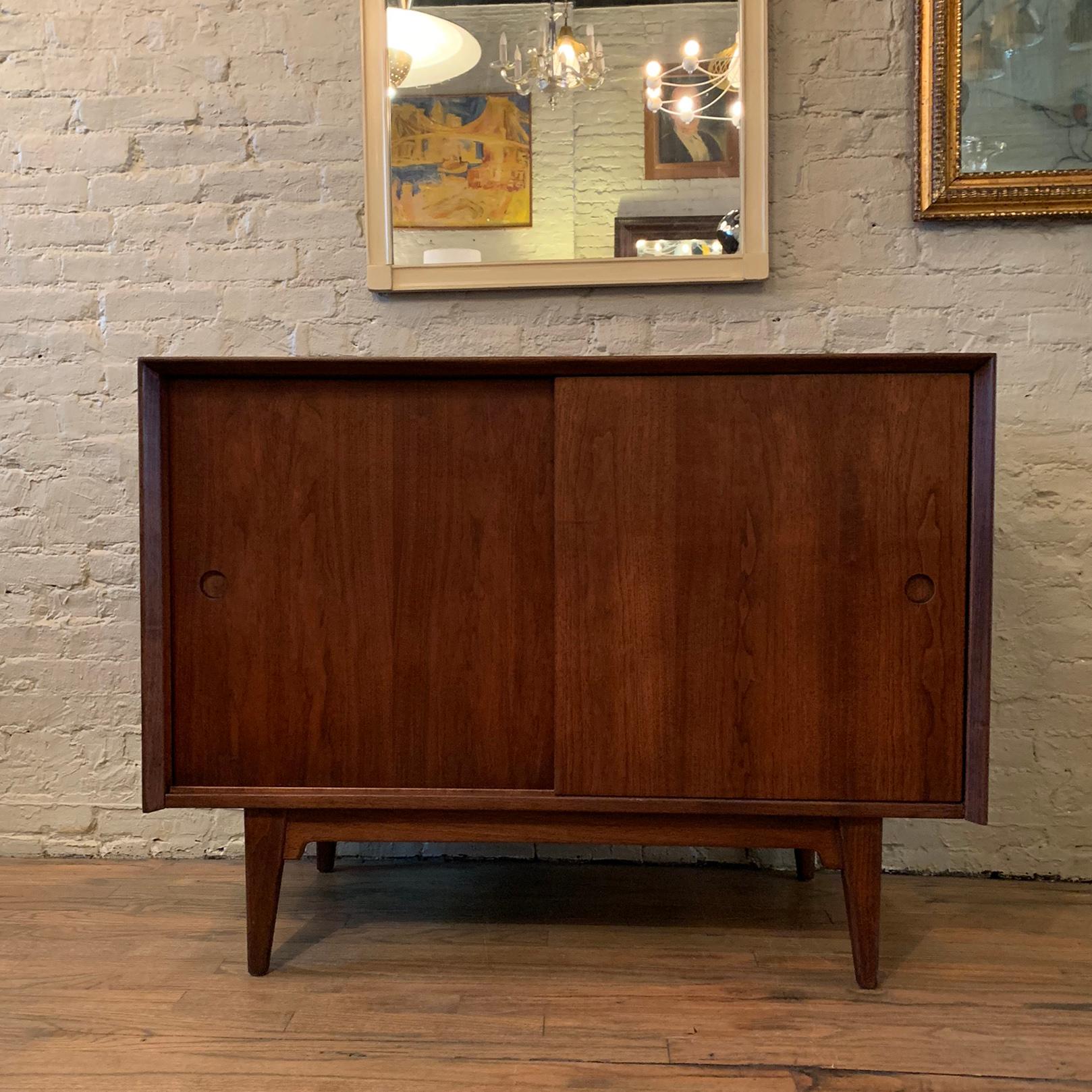 Elegant and minimal, Mid-Century Modern, walnut, credenza or sideboard cabinet by Jens Risom features recessed pulls on sliding doors with 2 interior shelves.