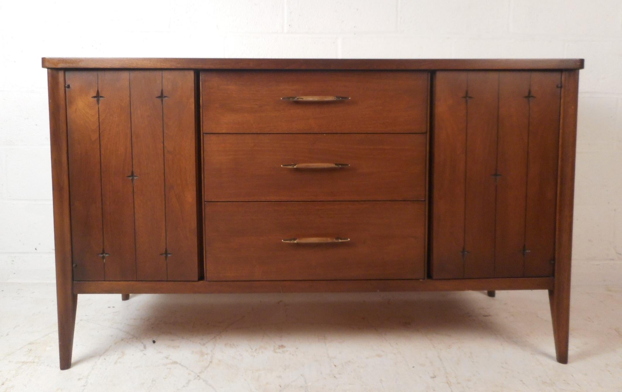 This beautiful vintage modern credenza provides plenty of room for storage within its three large drawers and two compartments hidden by cabinet doors. Sleek design with sculpted drawer pulls, etched designs on the cabinet doors, and tapered legs. A