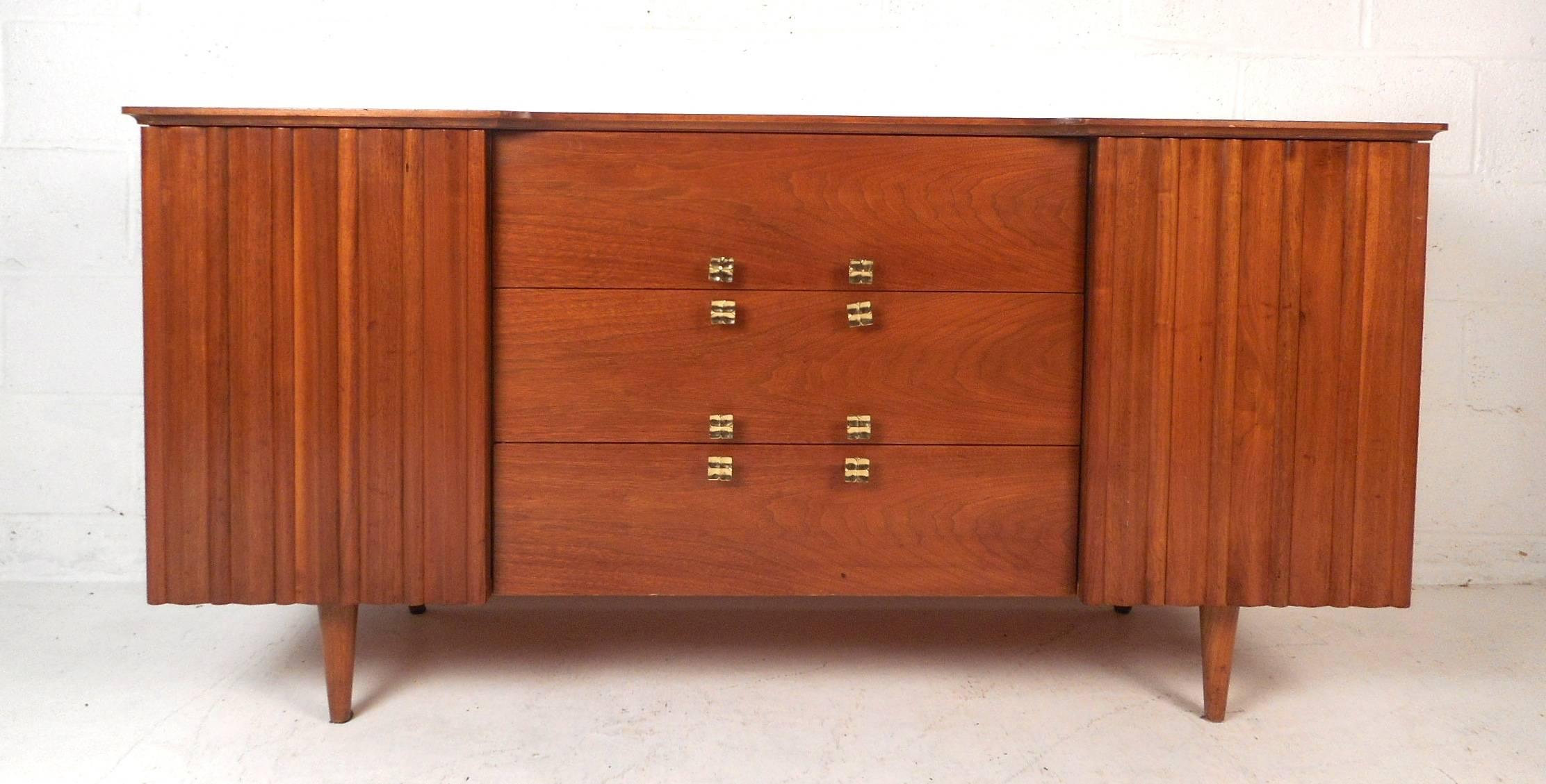 A fabulous vintage modern walnut credenza with two compartments hidden by cabinet doors, one hidden drawer, and three large drawers in the middle. This beautiful piece features unusual metal pulls, a sculpted top, and tapered legs. The cabinet doors