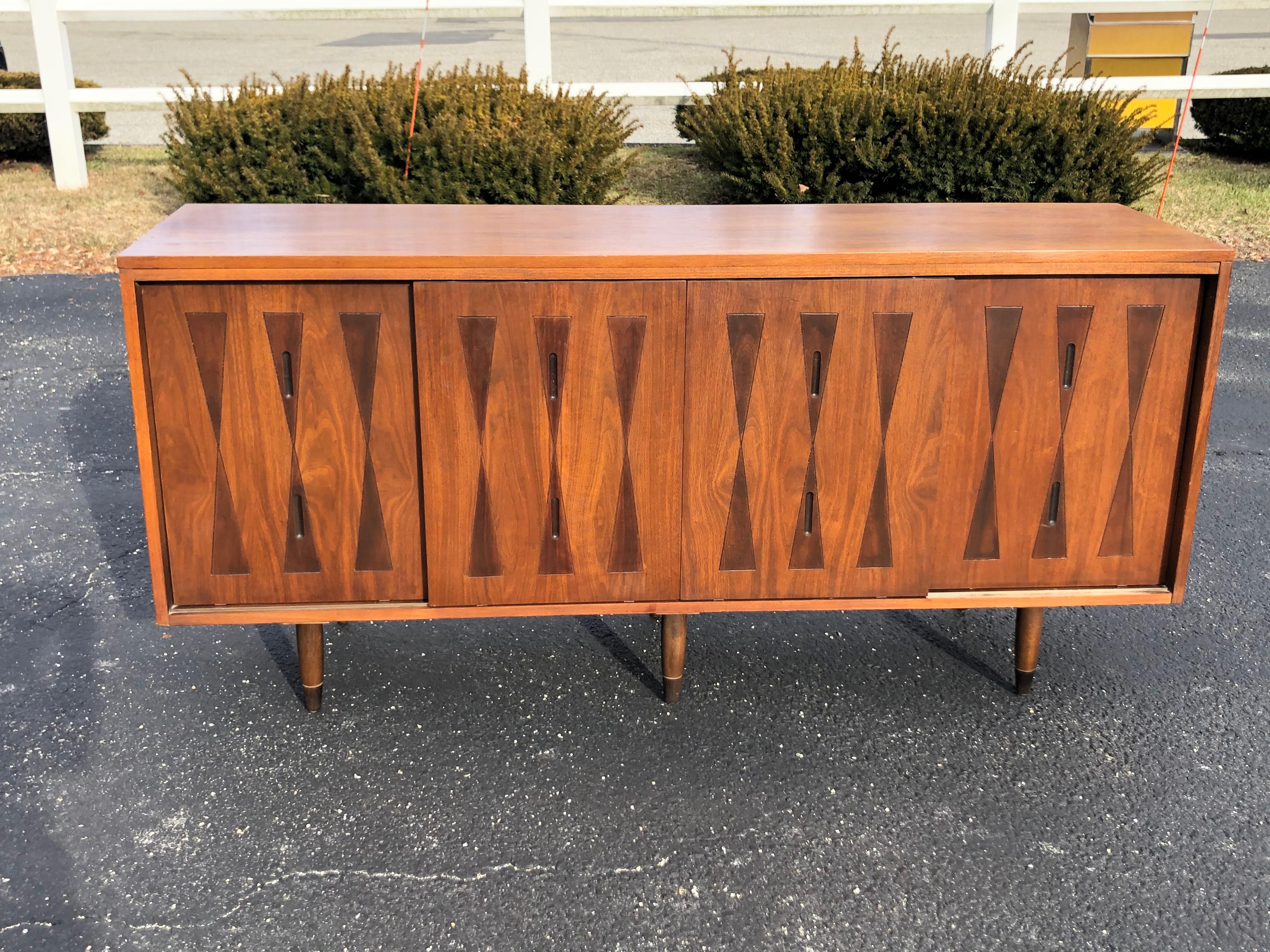 Mid-Century Modern walnut credenza. Unique two-toned harlequin pattern on four front doors. Four front doors slide on tracks to reveal interior shelving. Solid well built piece with 6 legs. It is rare to have two center support legs. So this is a