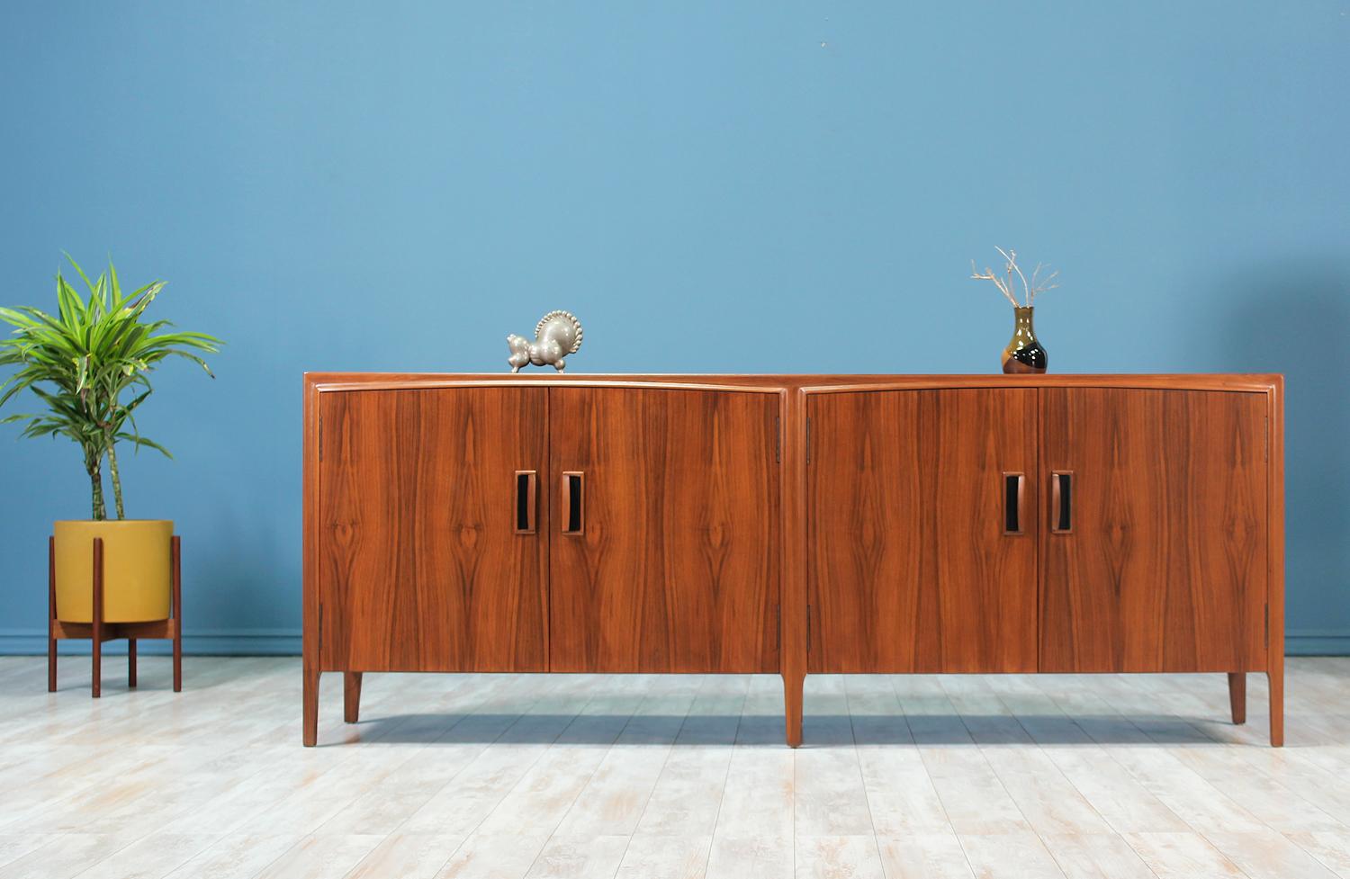 Stunning credenza manufactured circa 1950’s. This credenza features an elegant walnut wood case with with ample storage. The four pull-open front doors feature a slightly arched top, sculpted walnut pulls and panels of magnificent grain details. 