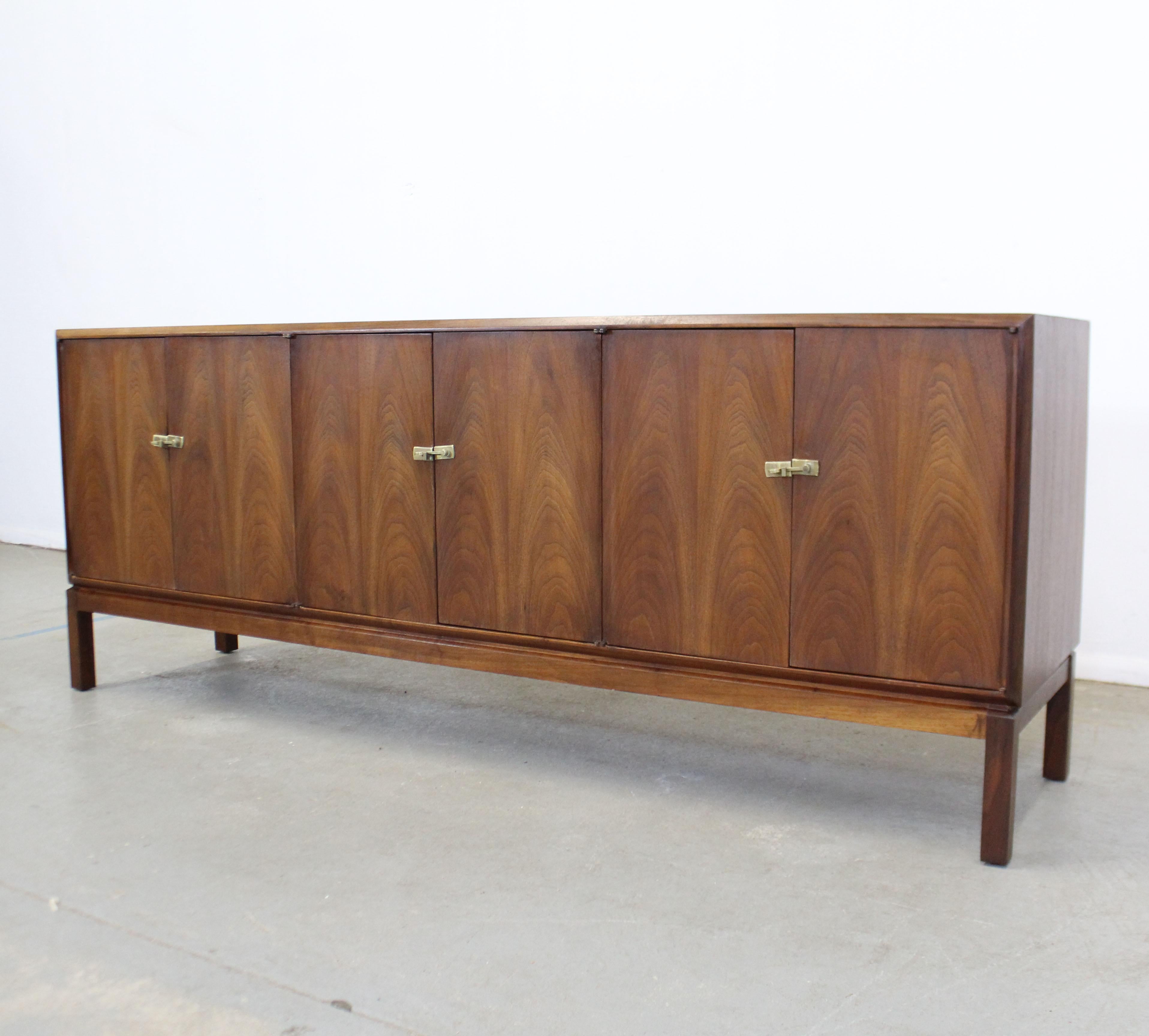Offered is a restored American Mid-Century Modern walnut credenza. The simple design is embellished with brass latches along the door fronts. Includes inner shelving and two center drawers. It is in excellent vintage condition, has been refinished