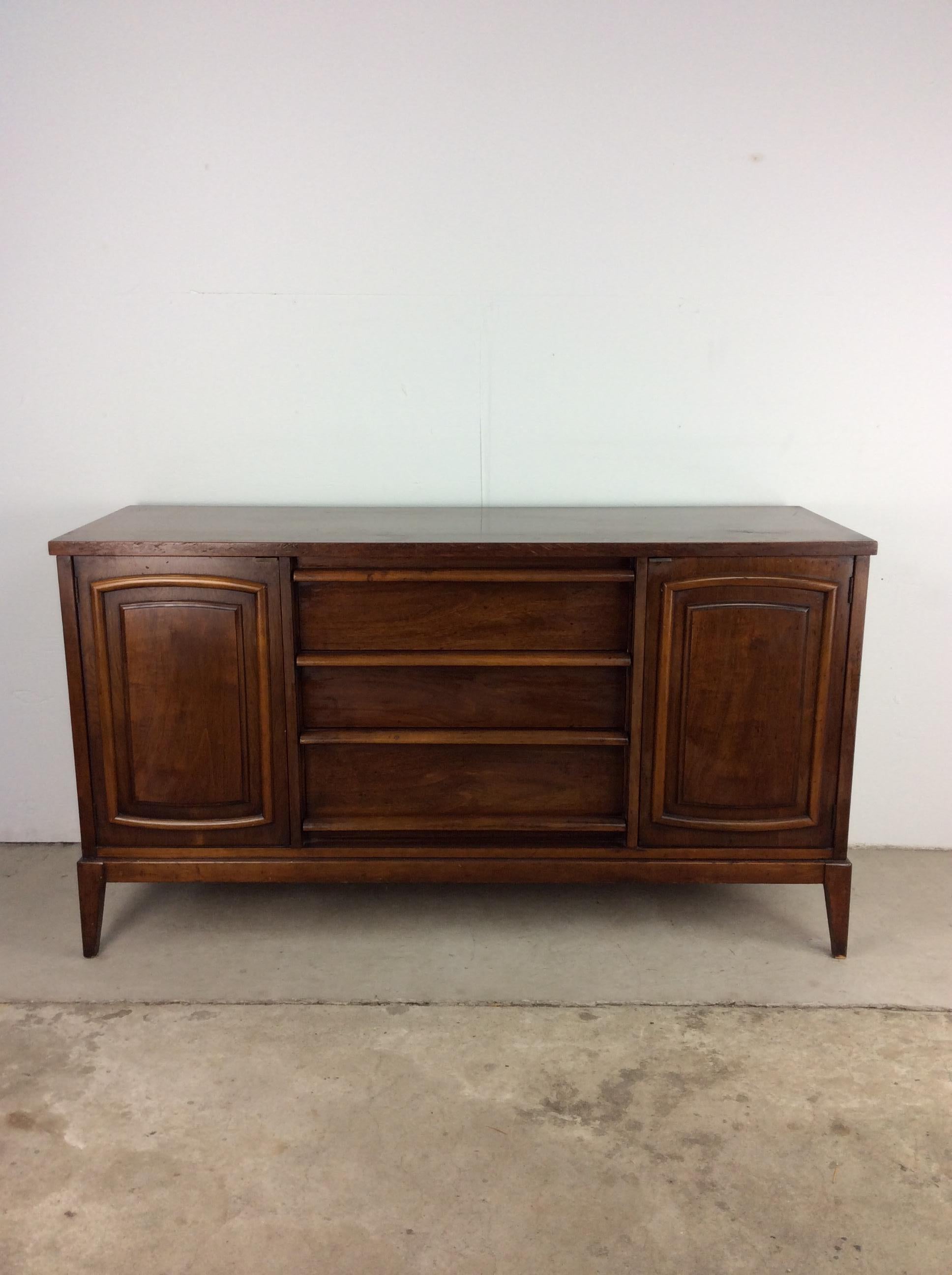 This mid century modern credenza / sideboard features hardwood construction, walnut veneer with original finish, three dovetailed drawers with sculpted wood pulls, two cabinets with single shelves, and tall tapered legs.

Dimensions: 56w 19d