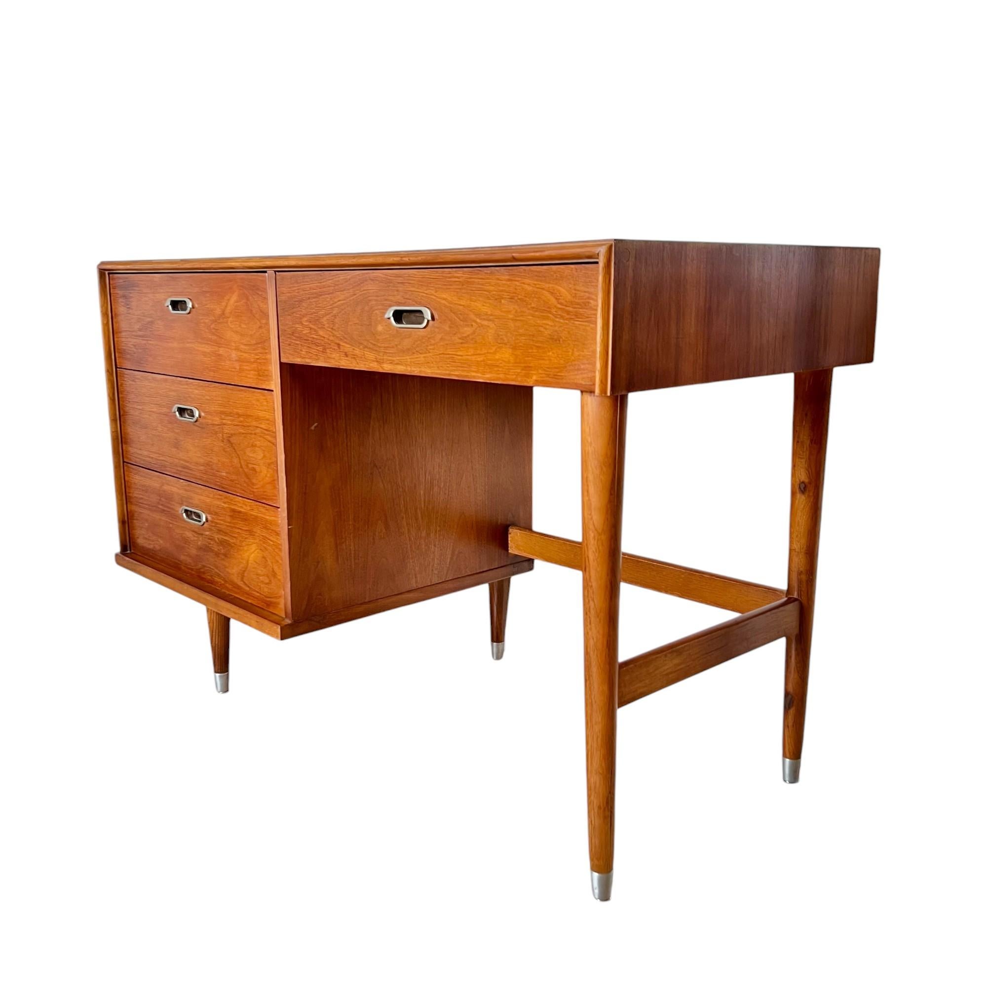 A classic mid-century modern single pedestal walnut writing desk by B.P. John Furniture circa 1969. It features three pedestal drawers, one writing utensil drawer with tray, gorgeous walnut veneer, five tapered legs, side and back stretchers, and
