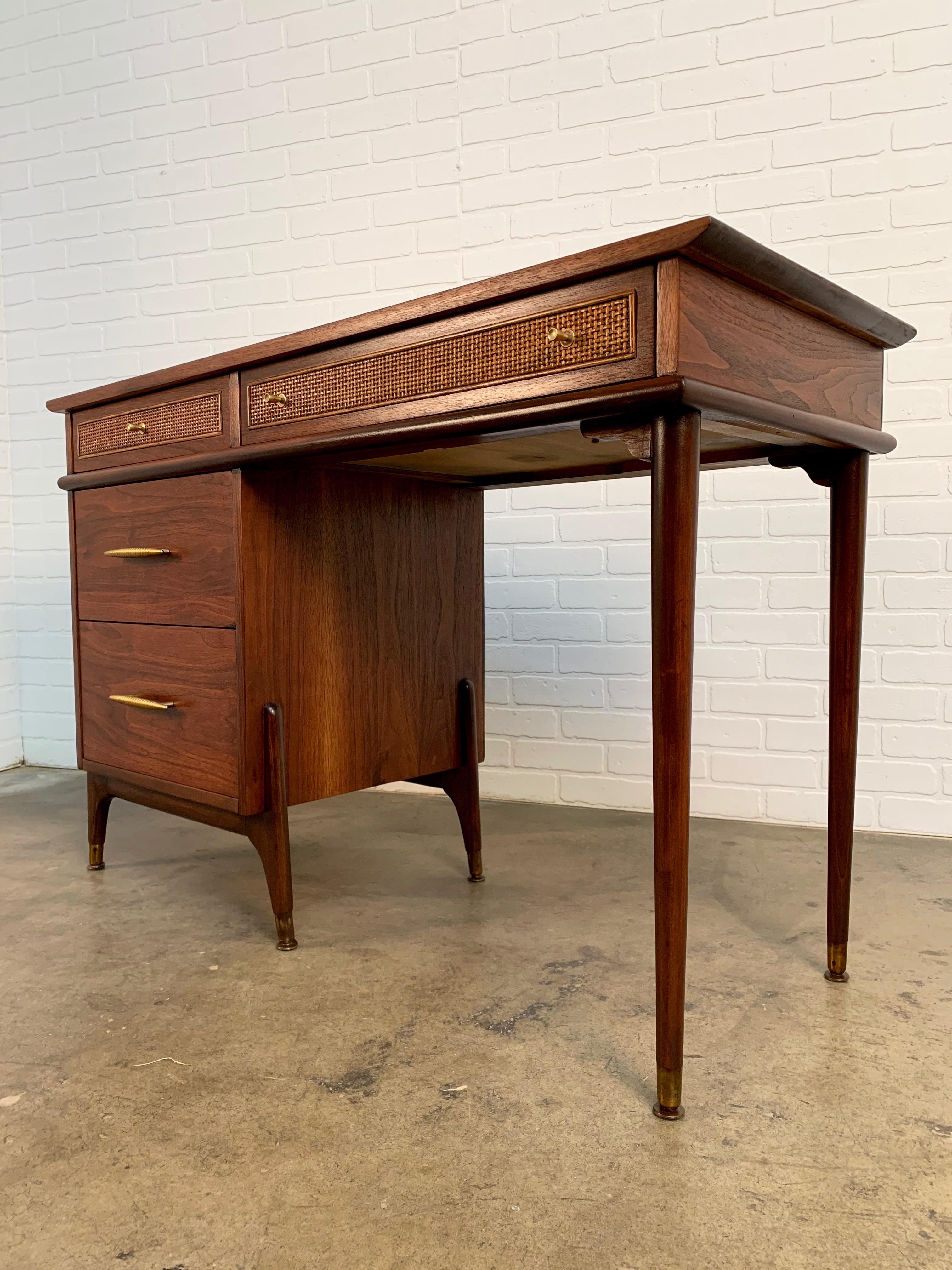 A combination of sculpted solid wood and walnut veneer with cane drawer front pane also brass finish drawer pulls. Can be used as a vanity. Knee height 24.63.