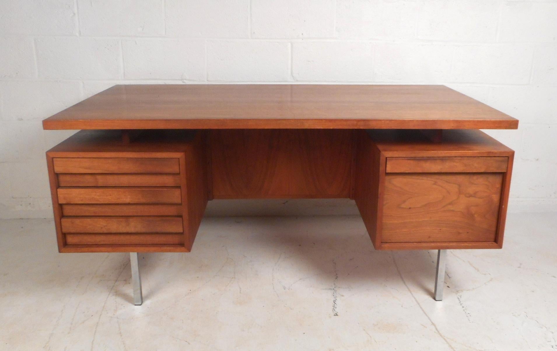 This beautiful desk features a vintage walnut finish and a large floating top for plenty of workspace. The desk is equipped with unique sculpted pulls on the four drawers and a finished back that comes with extra storage space. A sleek and sturdy