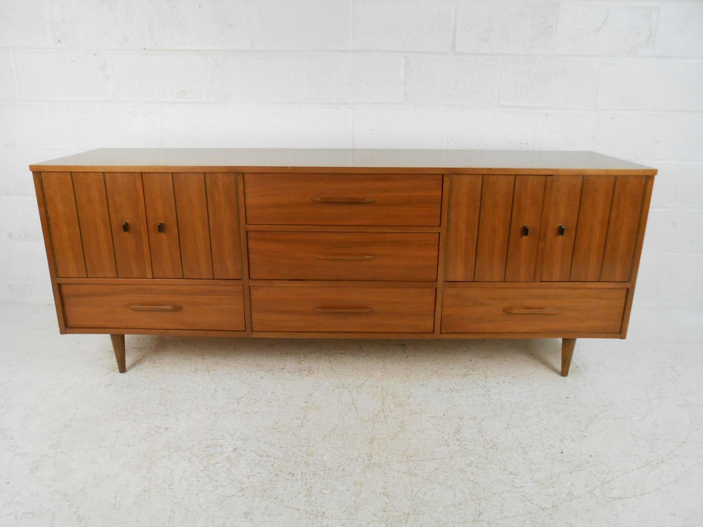 This stunning Lane style midcentury dresser offers plenty of room for storage within its nine hefty drawers. A sleek design with cabinet doors on each side that hide additional drawers. The sculpted wood drawer pulls, unusual ebonized cabinet pulls,