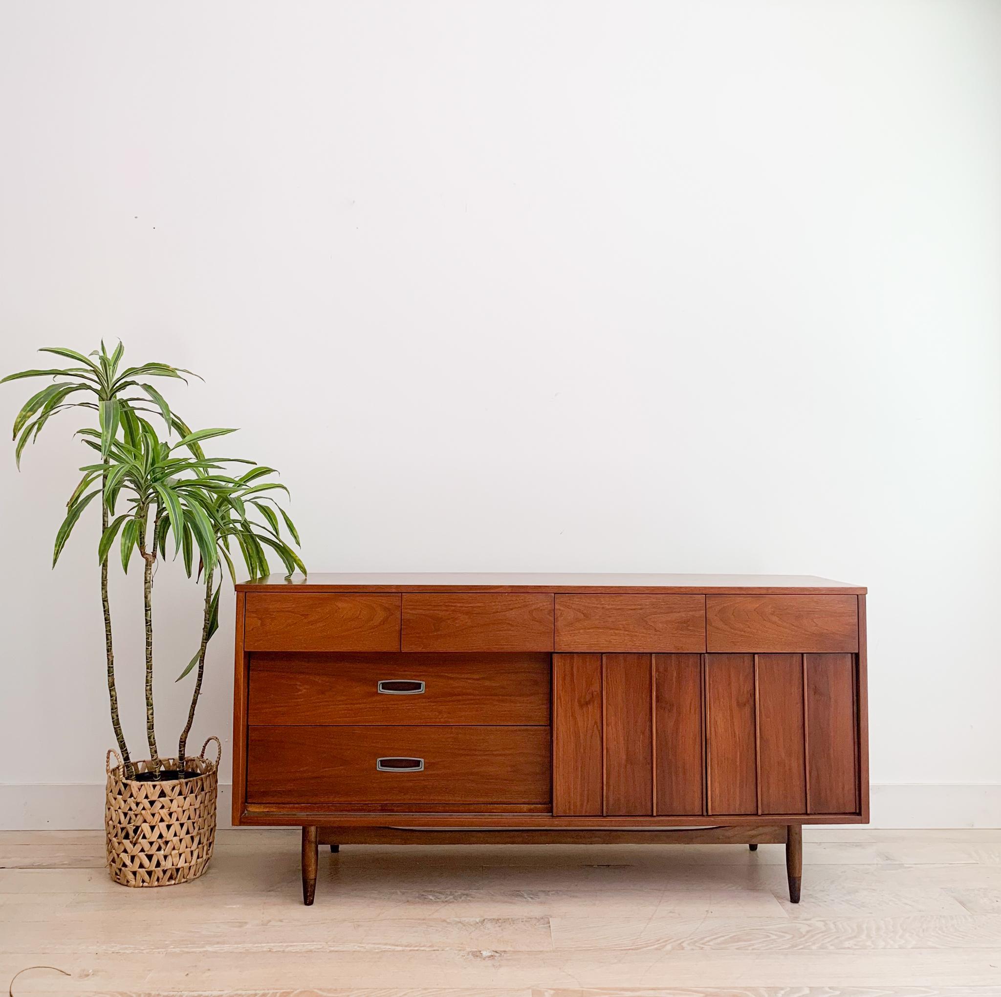 Introducing a beautiful mid-century modern walnut dresser by Mainline for Hooker Furniture, featuring sliding reversible cabinet doors. This dresser is in good condition, with some light scuffing, scratching, and small areas of veneer repair