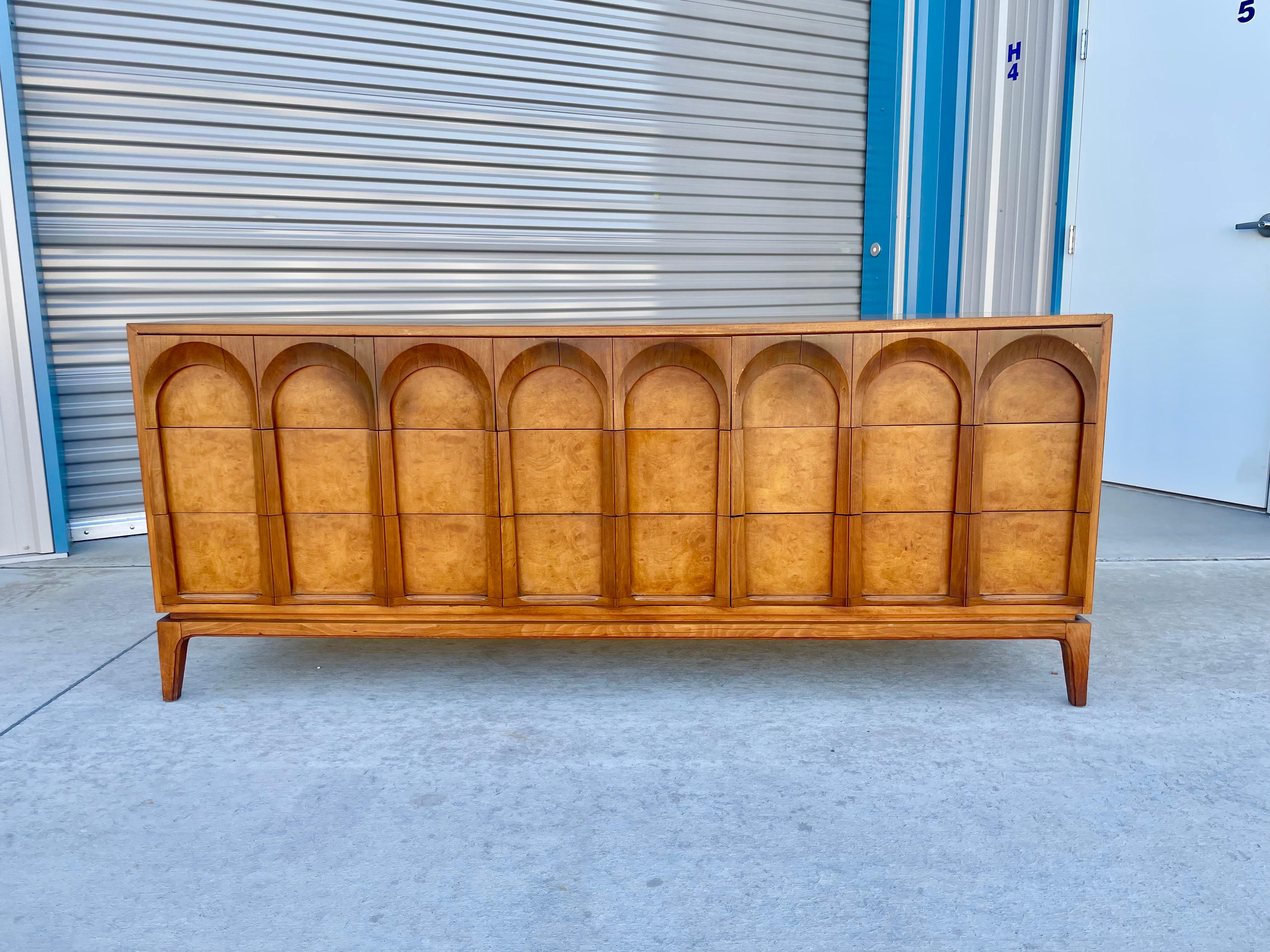 This stunning mid-century dresser was manufactured by Thomasville circa 1960s. This stunning piece features gorgeous walnut grain with burlwood inserts and sculpted cathedral arches, making it unique. The dresser also features nine pull-out drawers