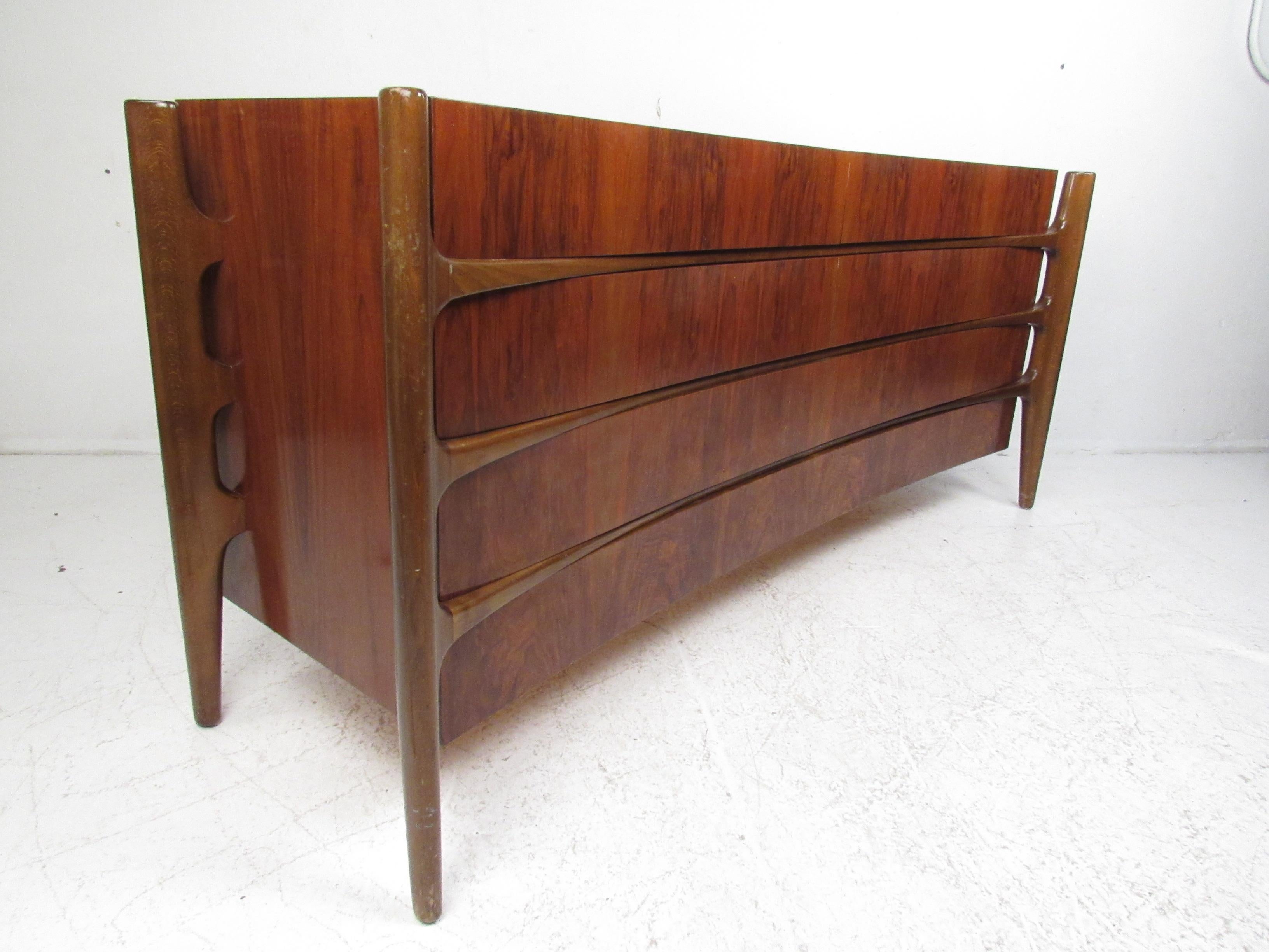 This impressive vintage modern dresser boasts a concave sculpted front design with edge mounted legs and an elegant walnut finish. A highly sought after, unique midcentury case piece that is sure to leave a lasting impression in any setting. The