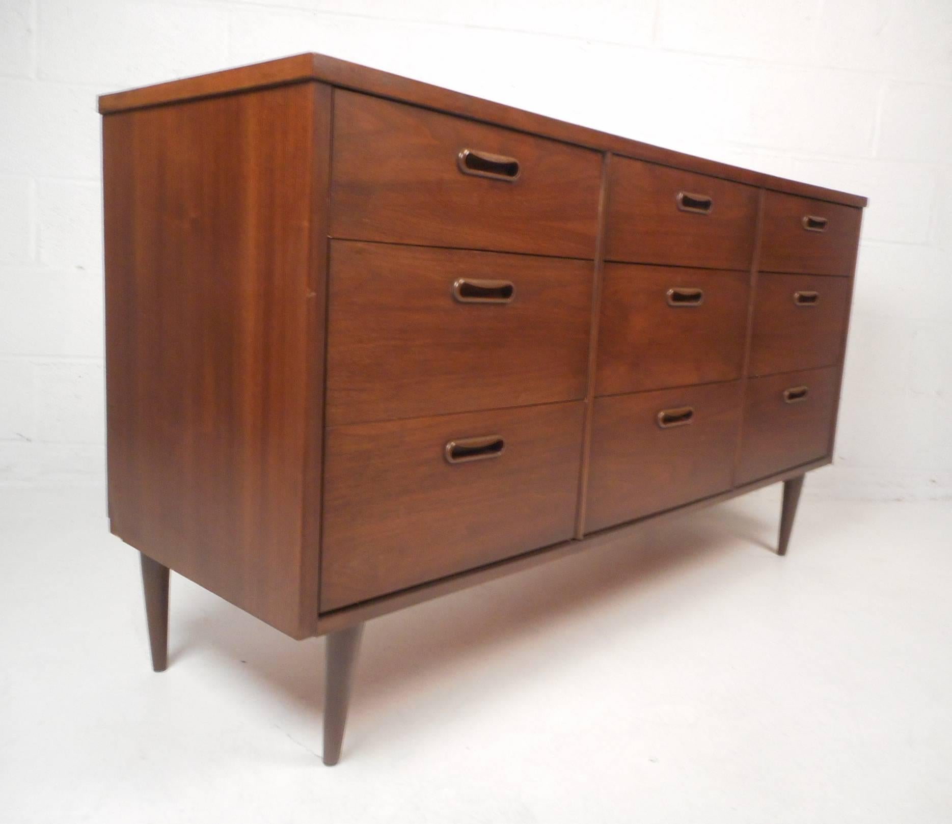 This beautiful vintage modern dresser provides plenty of room for storage within its nine hefty drawers. Sturdy construction with tapered legs, carved drawer pulls, and an elegant dark walnut finish. This stylish midcentury case piece makes the