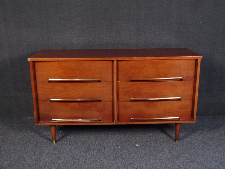 This vintage modern sturdy walnut chest of drawers features brass inlays and inset drawer pulls. Its straightforward design and tapered brass-capped legs are sure to fit in any modern home. Confirm pickup location(ny/nj).