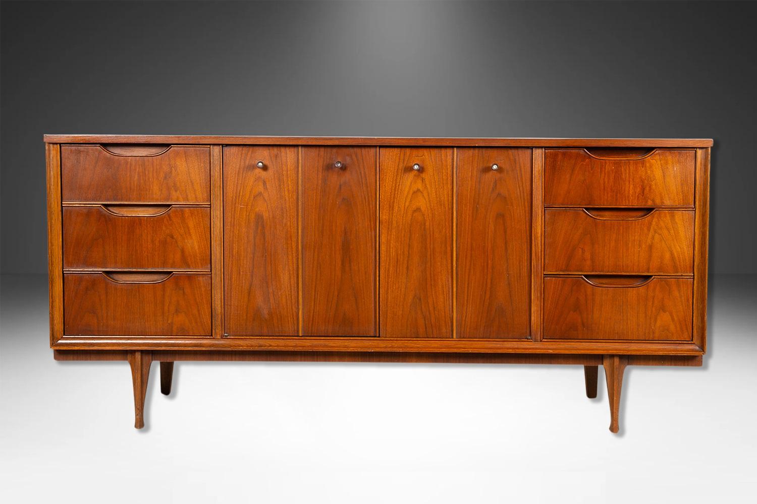 Un classico comò o credenza tripla in noce del Mid Century Modern. Questo comò d'epoca in noce presenta sei cassetti a coda di rondine affiancati da due ante centrali che si aprono per rivelare altri tre cassetti interni; il cassetto superiore è