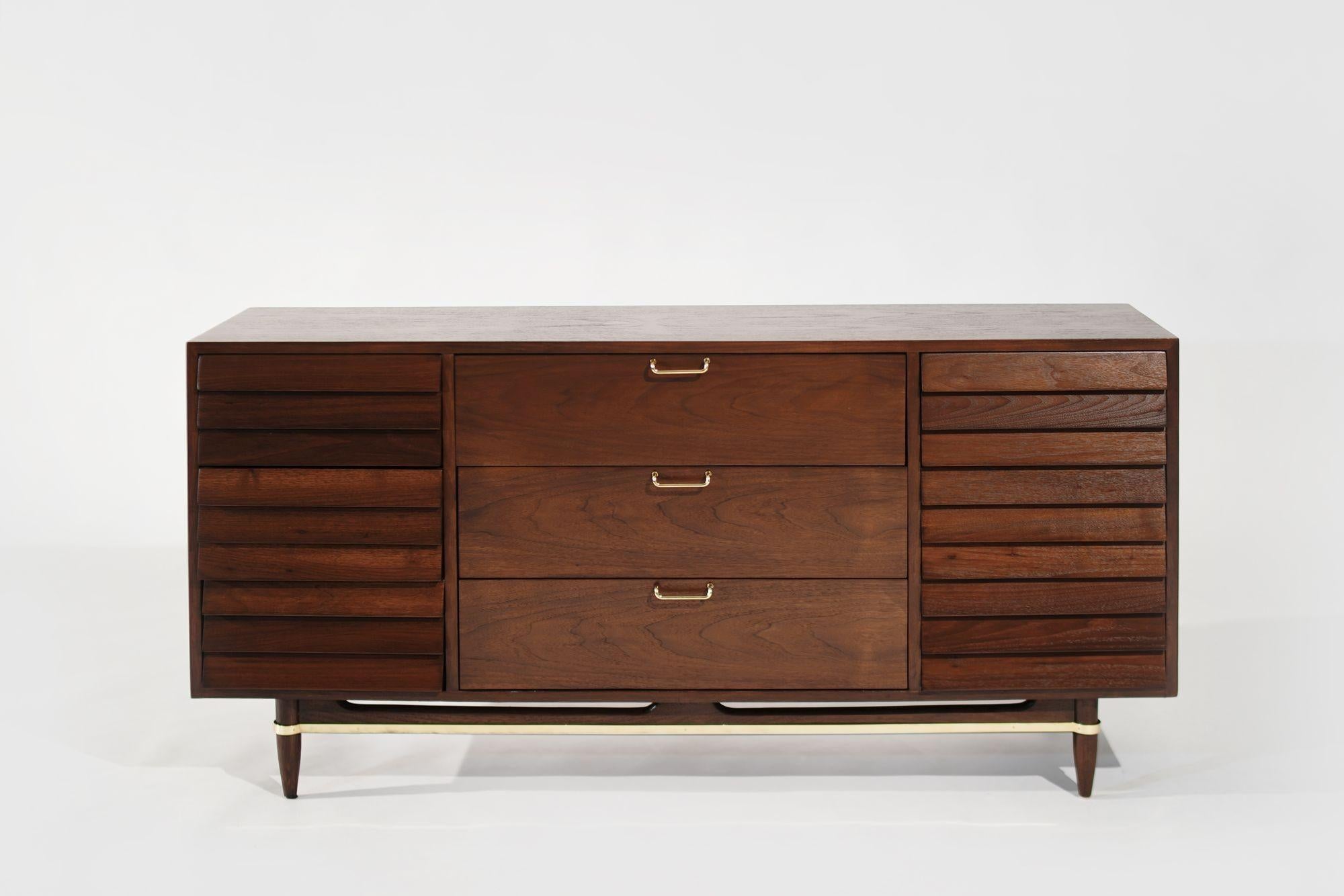A meticulously restored mid-century modern walnut dresser by American of Martinsville. Crafted with exquisite attention to detail, this piece features lustrous brass accents that beautifully complement the rich walnut wood. With nine spacious