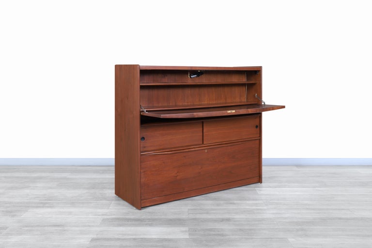 Beautiful Mid-Century Modern walnut dry bar manufactured and designed in the United States, circa 1960s. This bar has a conservative design that deceives the viewer and then surprises them by discovering the mysteries hidden in each area of its