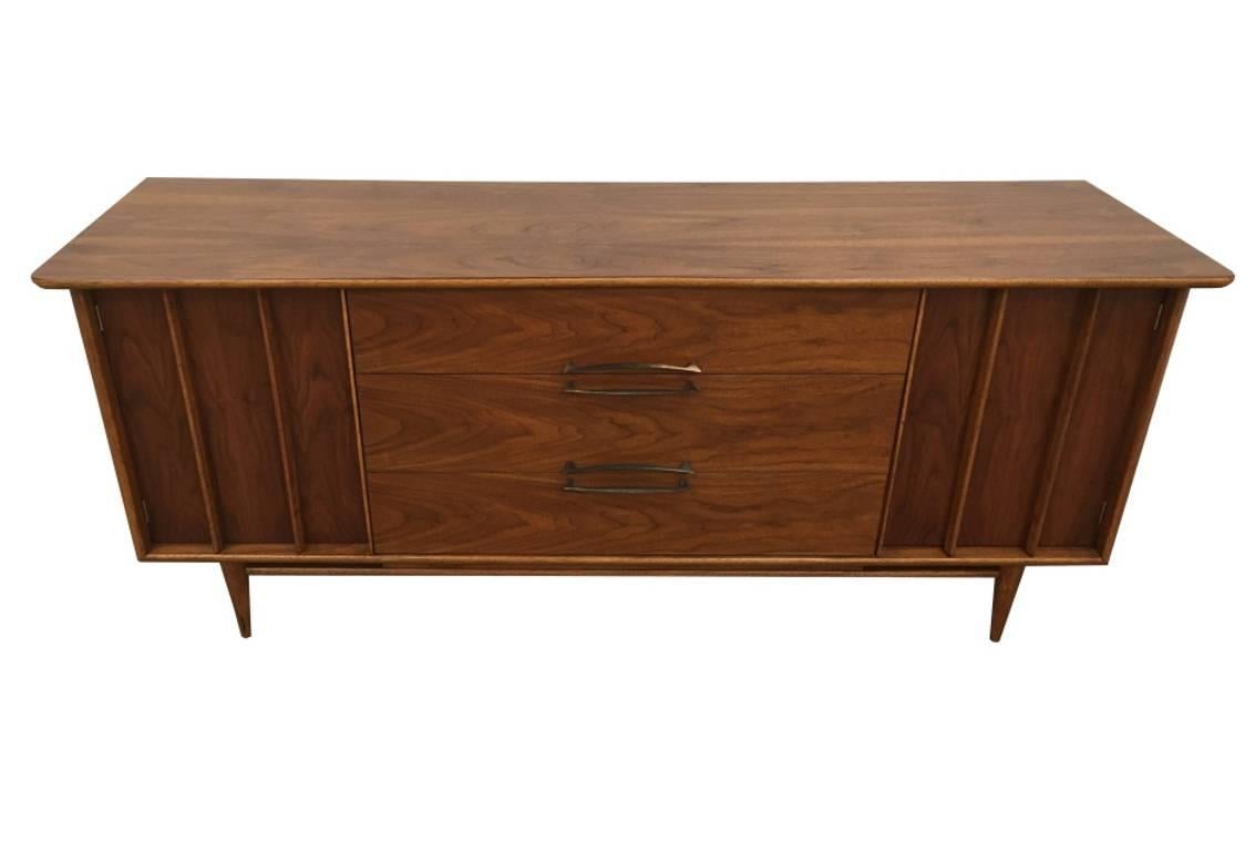 Beautiful walnut credenza from Kent Coffey. Features an angled/curved top with gorgeous wood grain. Two doors on either side that conceal three small drawers each. Three larger drawers in the centre for plenty of storage! Curved brass pulls.