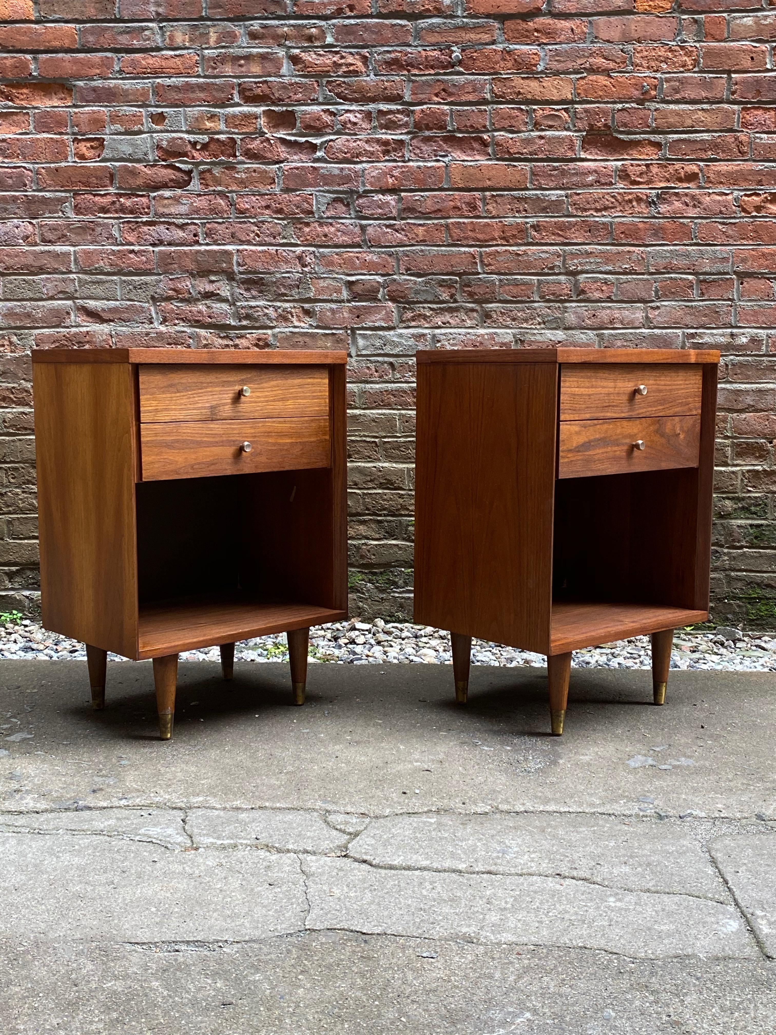 Walnut two drawer end tables with solid brass knobs. Signed with the enamel John Stuart retailer's tag, circa 1960. Nicely figure walnut veneers. 

Good old refinished condition. One older small veneer repair (see photo). Marks to drawer interior.