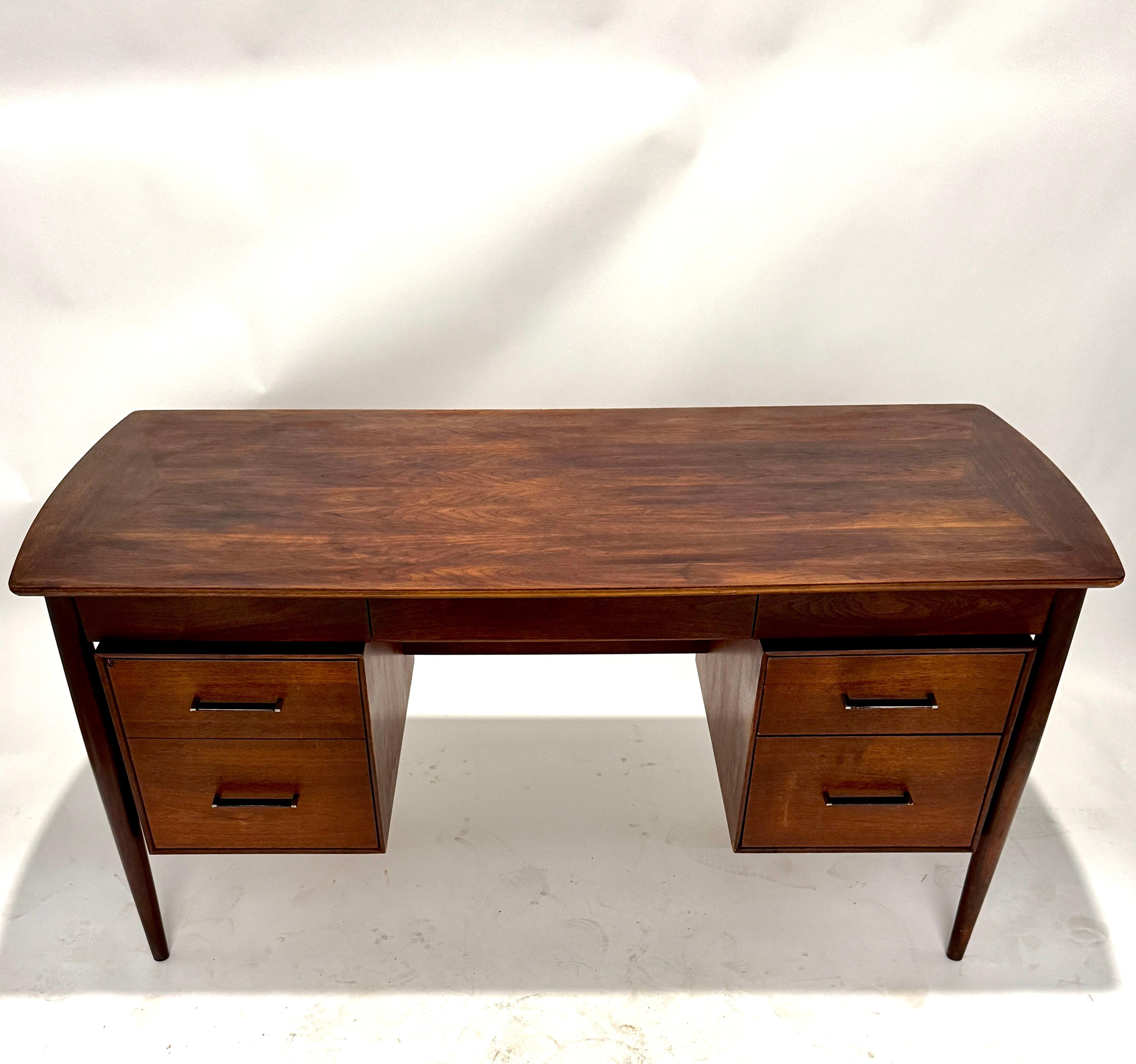 Elegante y escultural escritorio ejecutivo de nogal de mediados de siglo de Ramseur Furniture Company, fabricado en Estados Unidos hacia la década de 1950. Esta pieza de fina construcción presenta un borde superior graciosamente curvado y patas