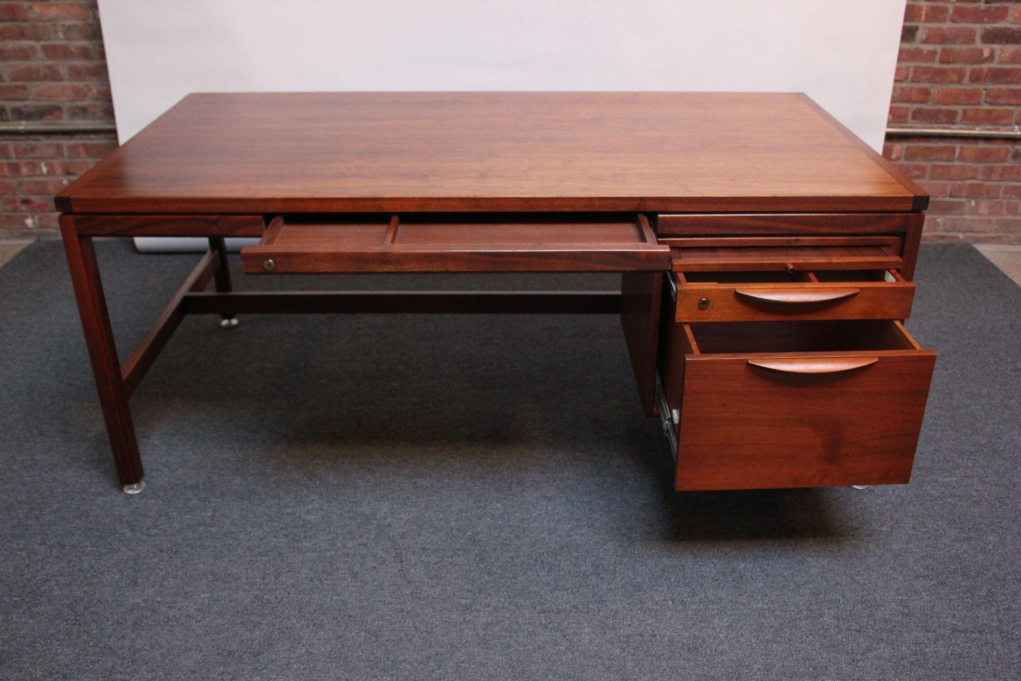 Mid-Century American Modern single pedestal executive desk in walnut by Jens Risom (ca. 1960, USA).
Features a pull-out writing surface with glass top above a drawer with a laminate surface flanked by a solid walnut divider atop a corresponding
