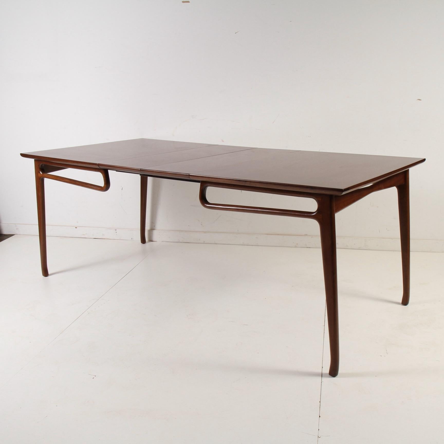 A rather rare 1950s vintage dining table with two leaves that was originally a pickled finish with black airbrushed accents. This great piece has been updated and refinished to display its walnut grain and to better highlight its Italian-influenced