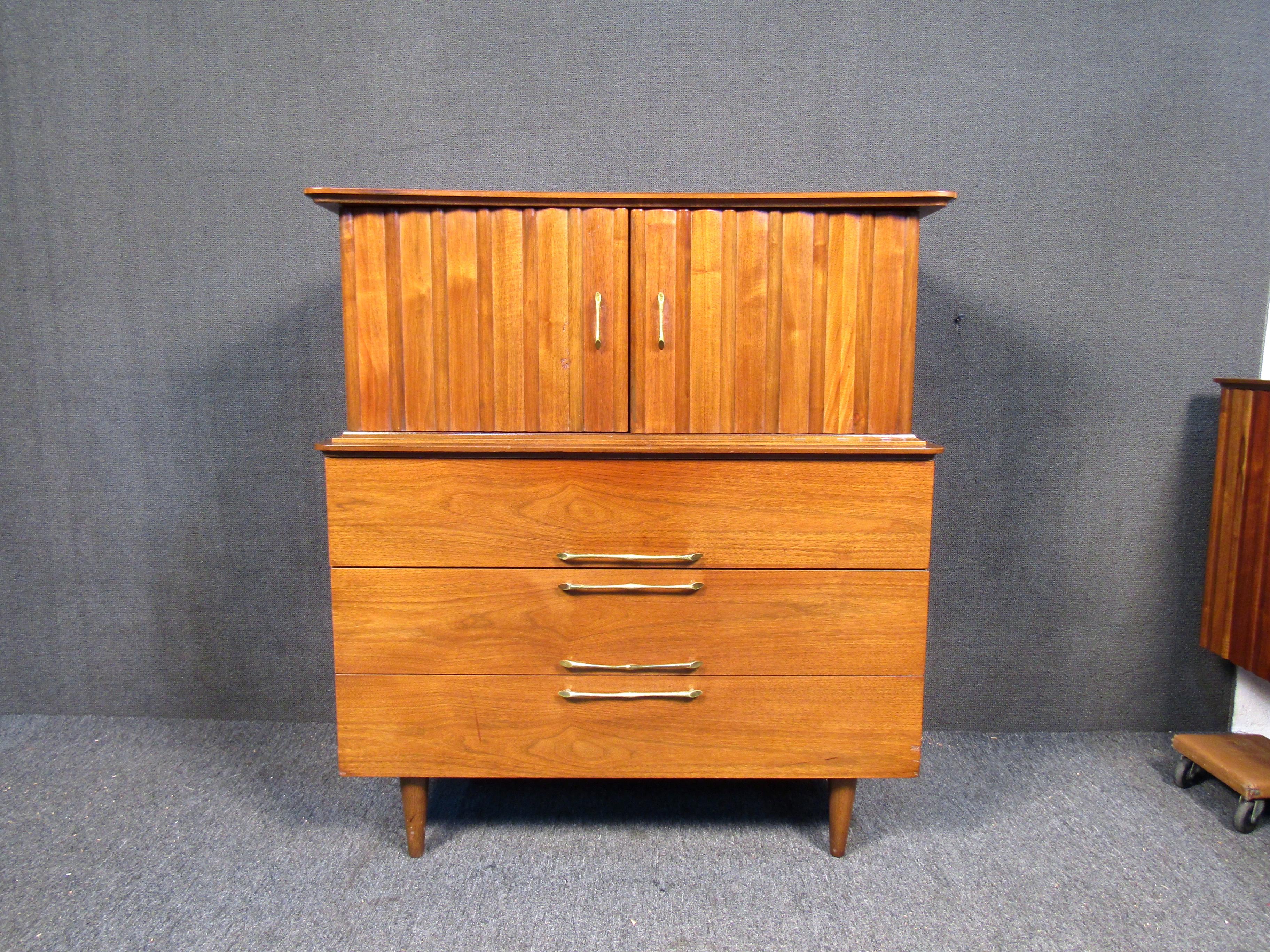 A Mid-Century Modern hi-boy dresser featuring two doors, seven drawers and a sleek walnut construction. This piece has unusual brass handles with walnut feet. The dresser will surely be a great addition to any living space.
Please confirm item