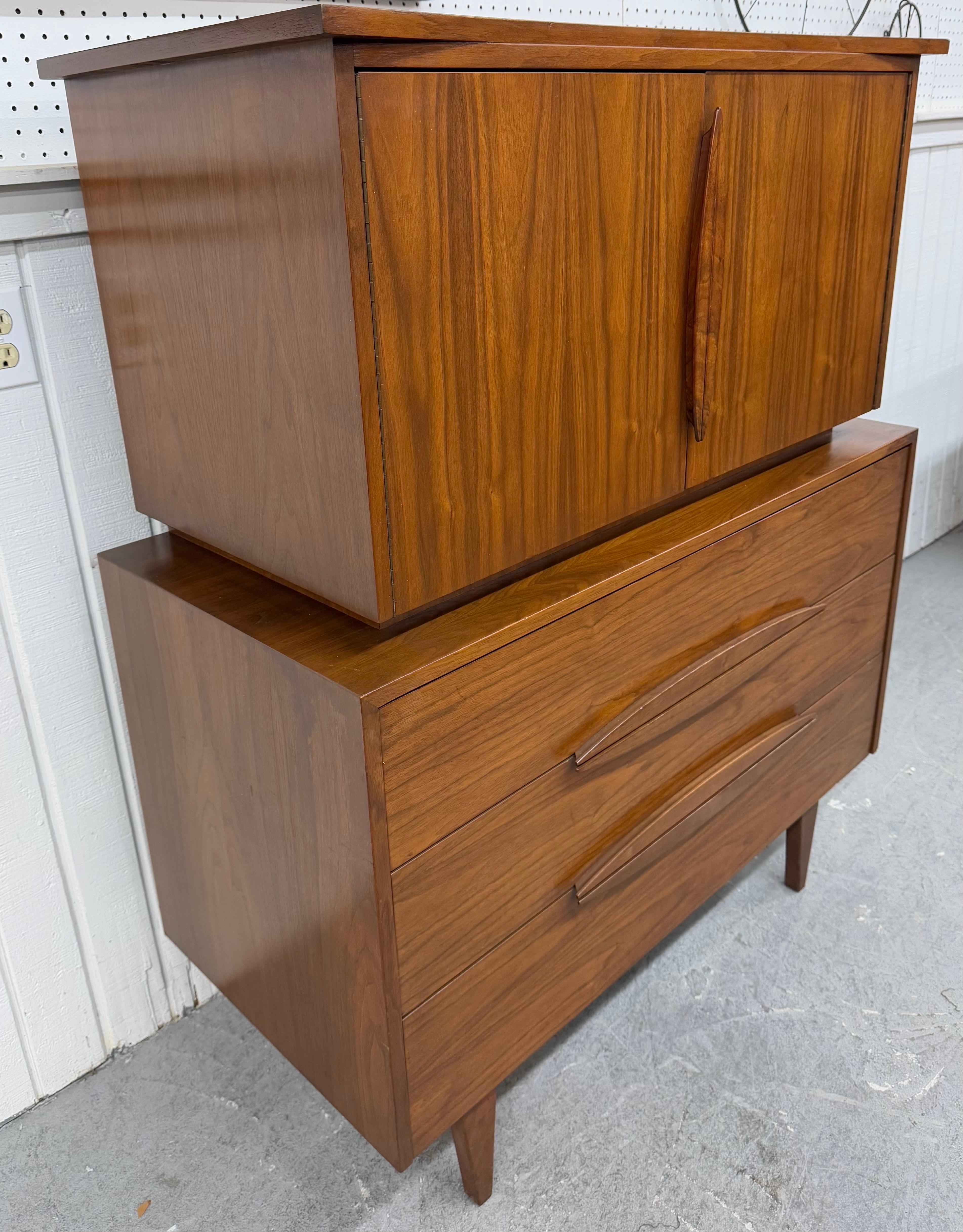 This listing is for a Mid-Century Modern Walnut High Chest. Featuring a straight line chest on chest design, two doors that open up to three hidden drawers, three larger drawers at the bottom, sculpted wooden pulls, modern legs, and a beautiful