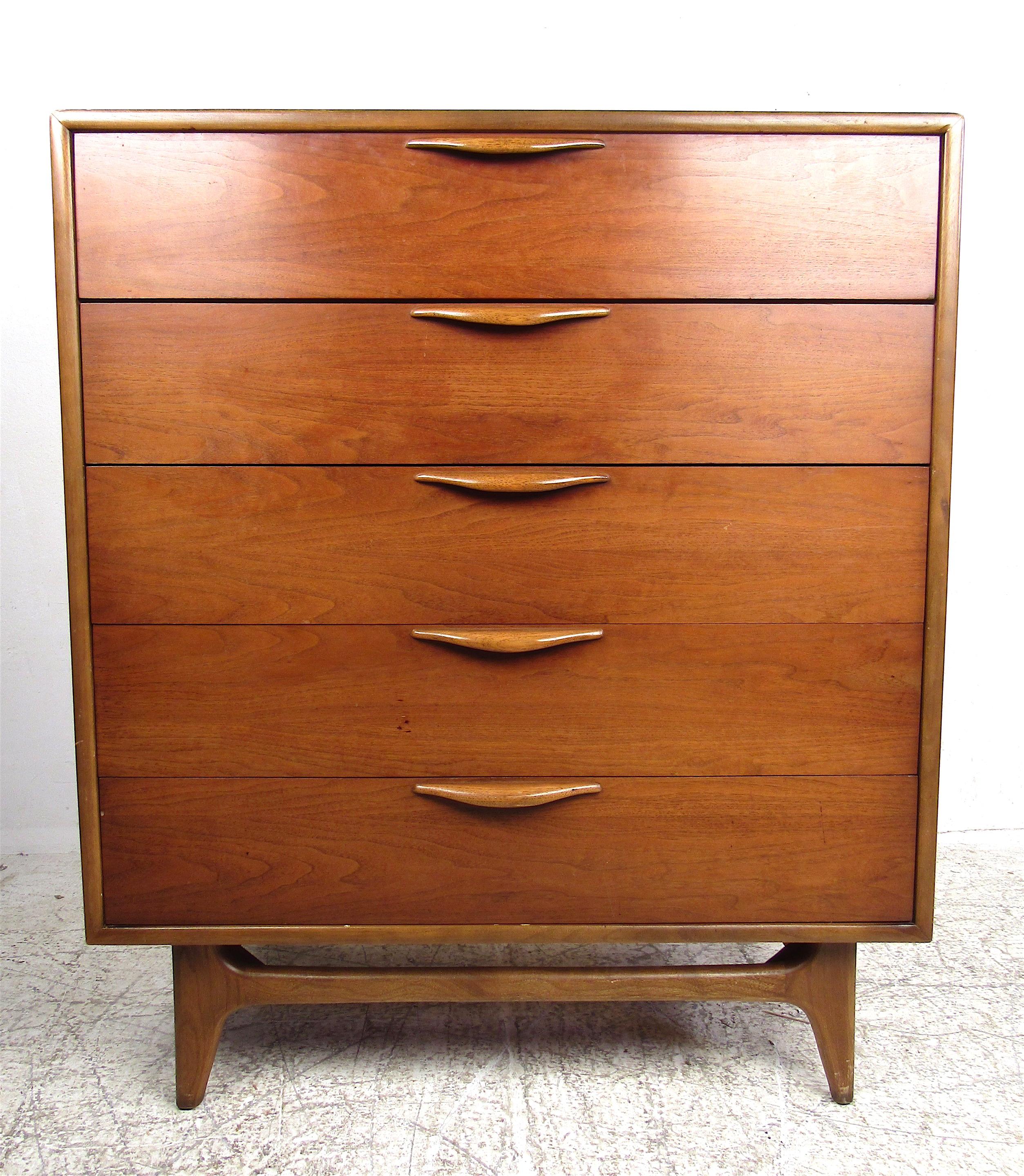 A stunning vintage modern highboy dresser with five hefty drawers for ample storage space. Elegant walnut wood grain, sculpted drawer pulls, and splayed legs add to the midcentury appeal. This versatile chest of drawers makes the perfect fit in any