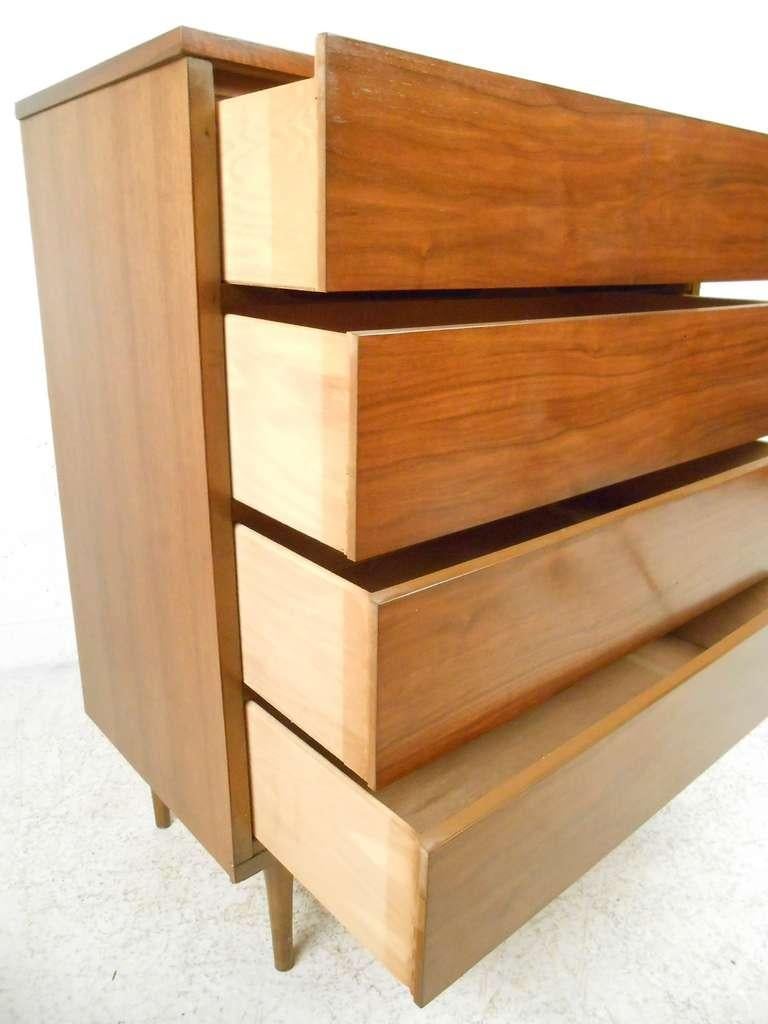 A beautiful vintage modern highboy dresser that features recessed drawer pulls, tapered legs, and a sleek Minimalist appearance. Please confirm item location (NY or NJ).