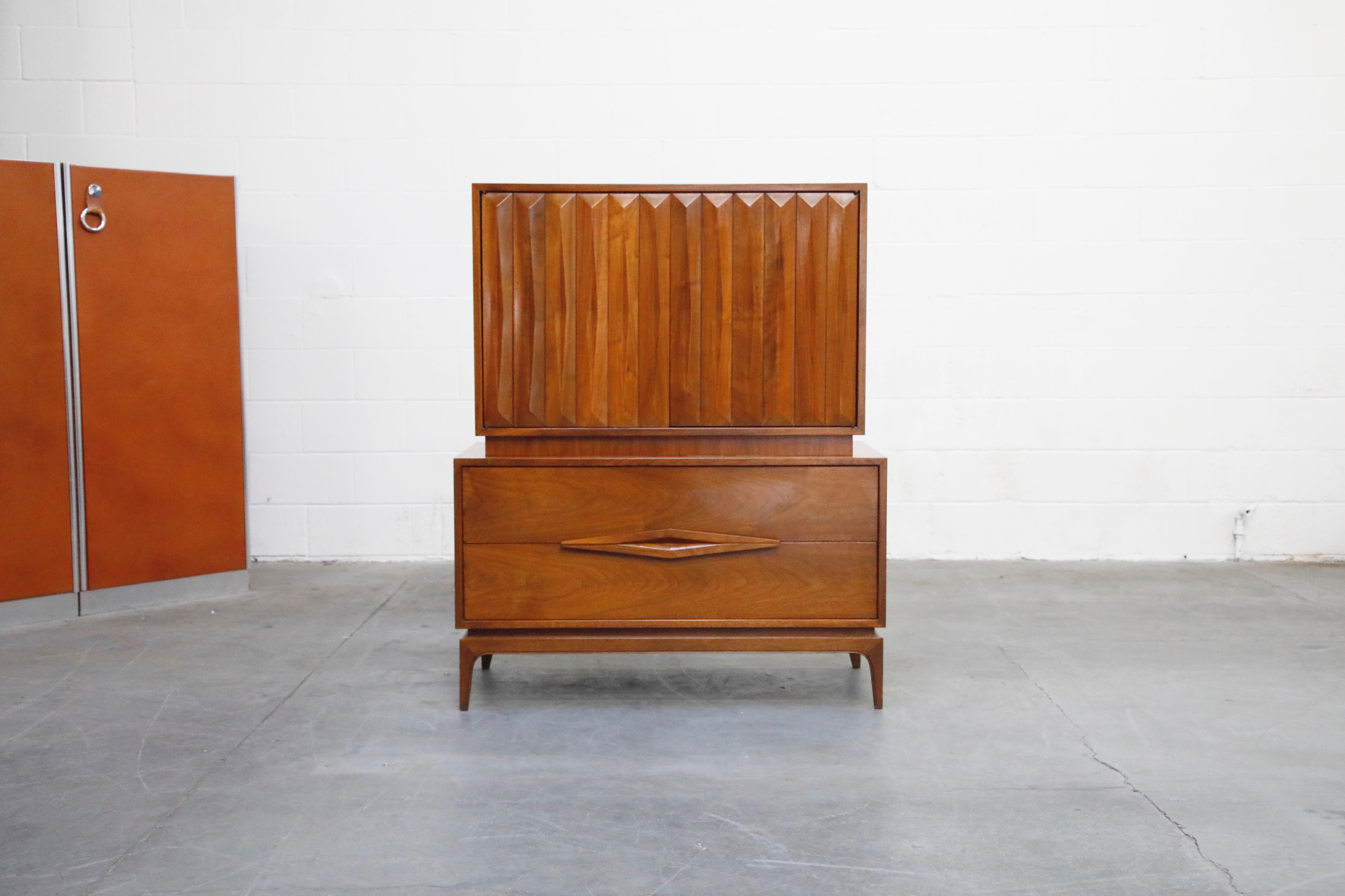 A lovely American Mid-Century Modern highboy dresser sculpted from Walnut featuring louvered styled doors and an artistic lower drawer pulls / handles. This beautiful highboy cabinet has 3 pull out drawers in the upper cabinet space which is hidden